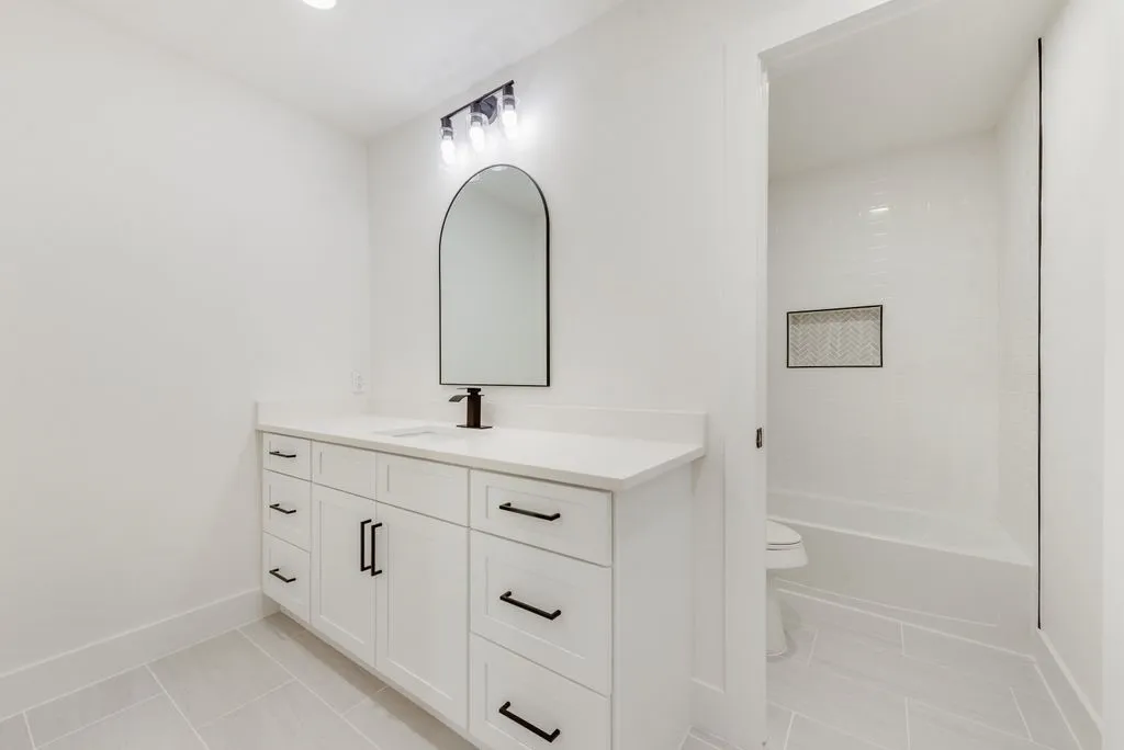 White vanity with black hardware, arched mirror, single basin sink, and a black faucet