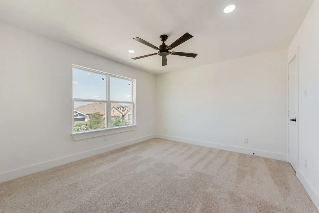 Spacious room featuring neutral carpeting, a large window, a ceiling fan with integrated lighting, and recessed ceiling lights