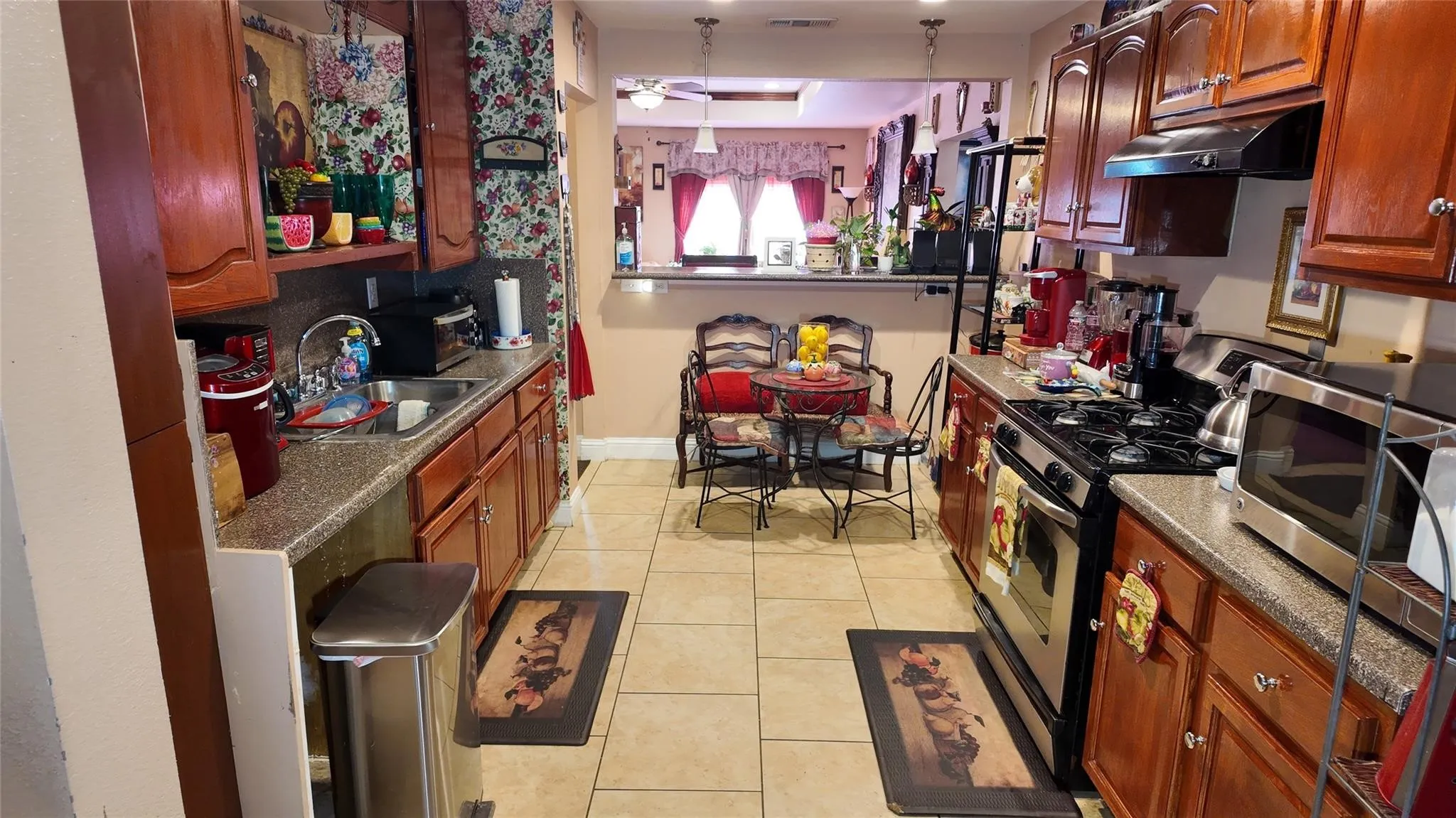 Galley kitchen featuring wood cabinetry, stone-look countertops, stainless steel appliances, and tile flooring