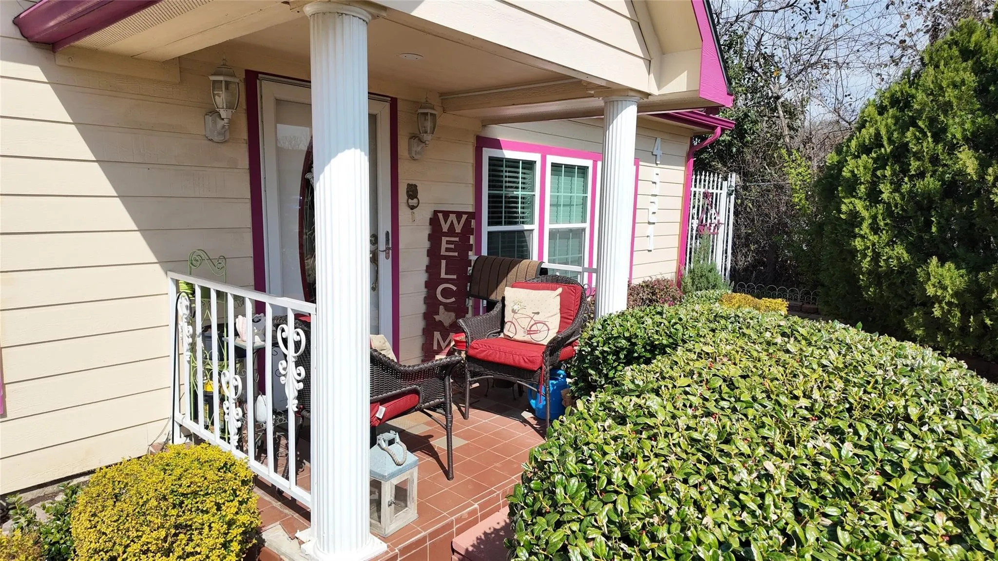 Covered front porch with fluted columns and white railing, brick-finish flooring, and exterior wall sconces