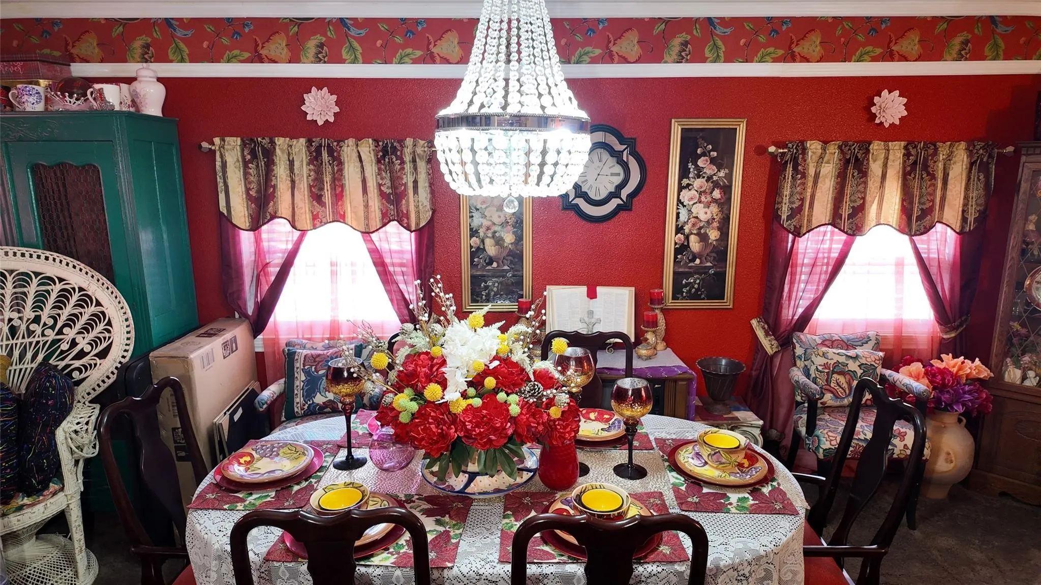 Decorative chandelier illuminating a dining area with a patterned wallpaper border, red walls, and window treatments