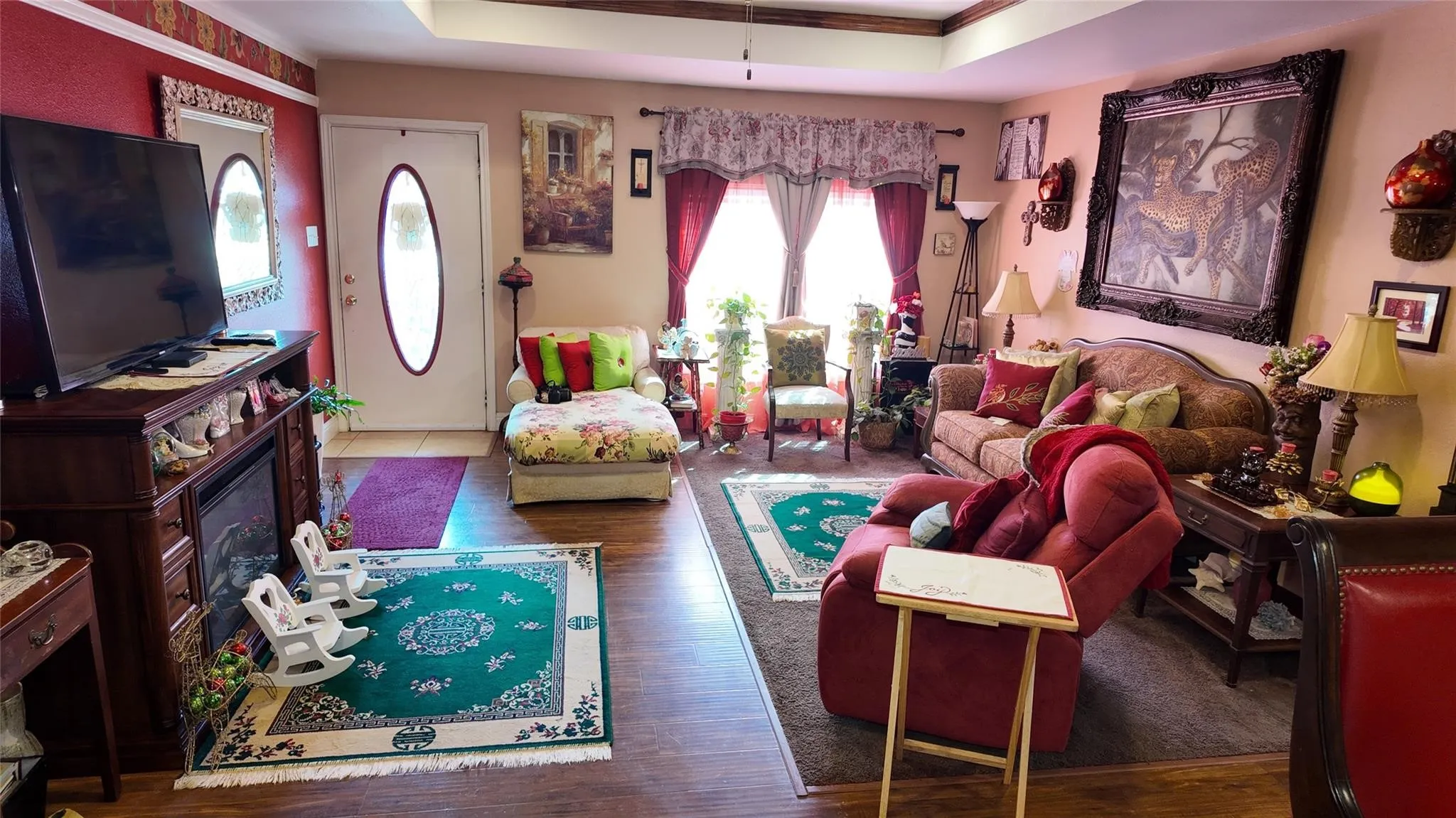 Wood-finish flooring, tray ceiling, integrated fireplace, wall-mounted light fixtures, decorative window treatments