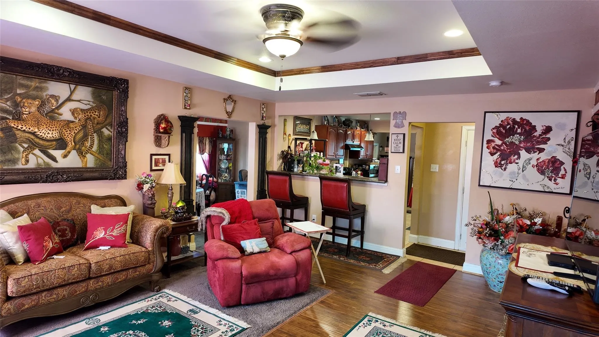 Recessed ceiling with wood-finish trim, ceiling fan with integrated lighting, wood-finish flooring, built-in breakfast bar with countertop, and overhead built-in cabinetry