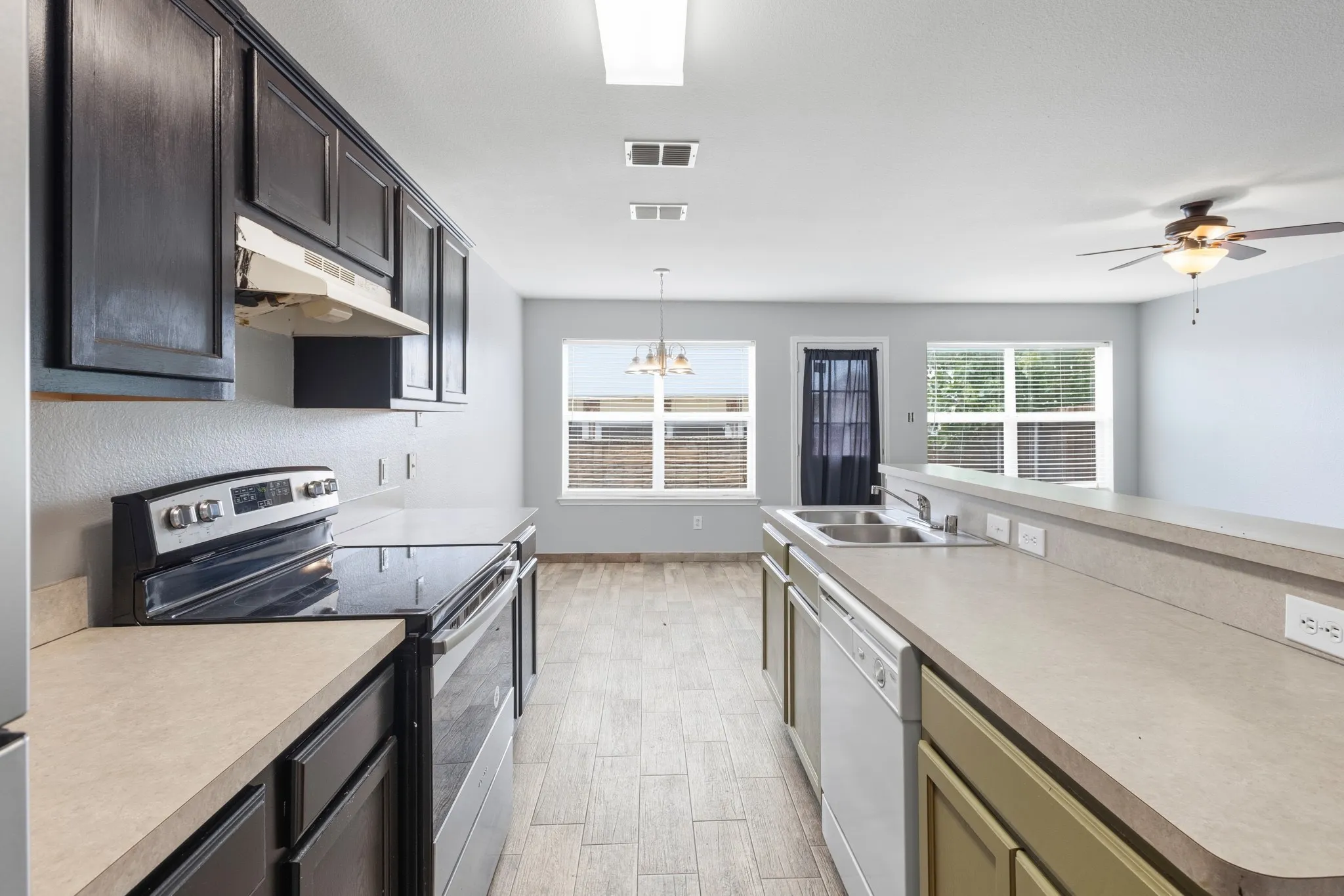 Galley kitchen featuring dark wood cabinetry, white appliances, and a pass-through counter with a double-basin sink
