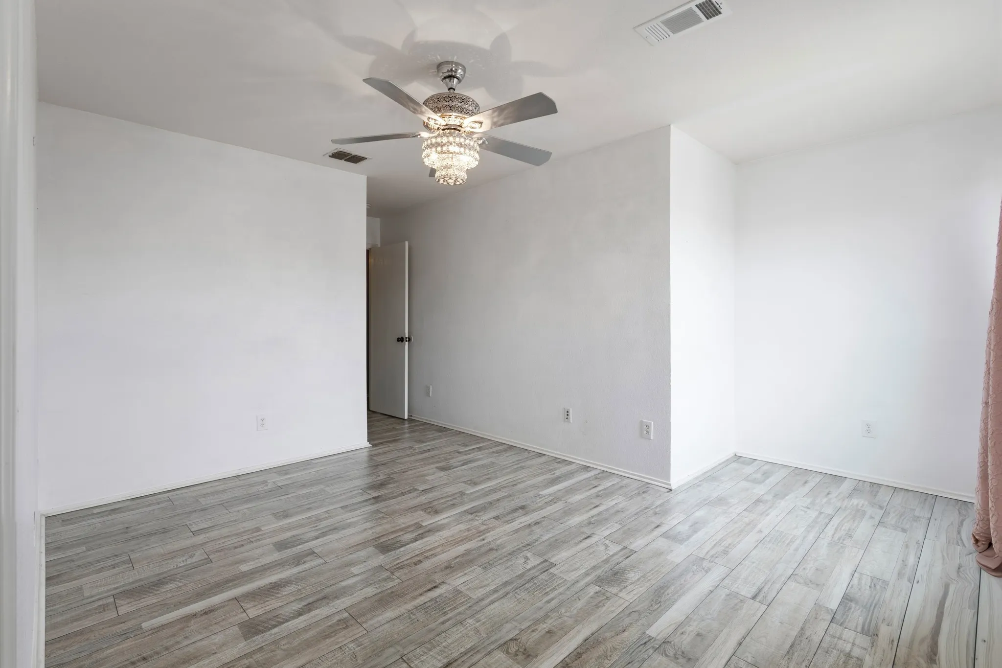 Wood-finish flooring, white walls, and a crystal chandelier ceiling fan