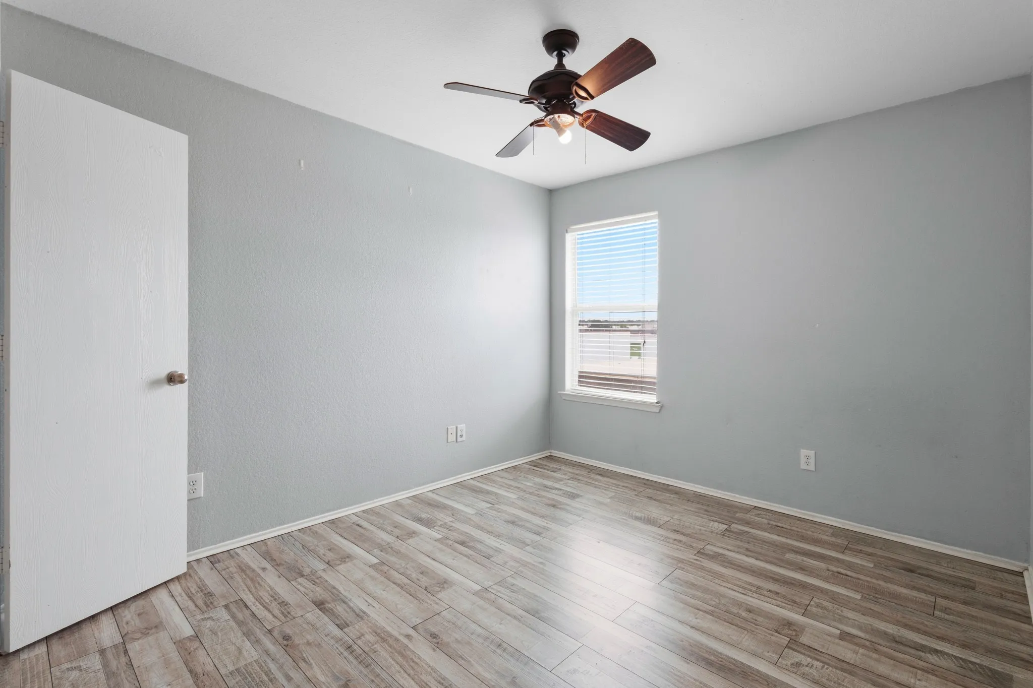 Light gray walls, wood-finish flooring, and a ceiling fan with integrated lighting