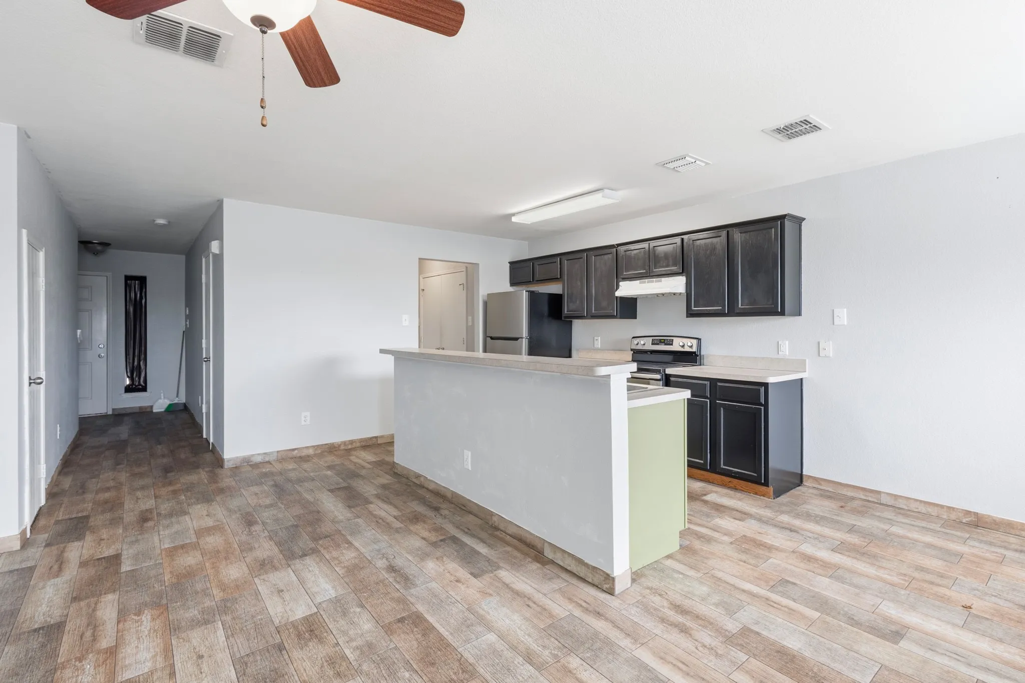 Open concept living space featuring wood-finish flooring, a kitchen island with a breakfast bar, dark cabinetry, and stainless steel appliances