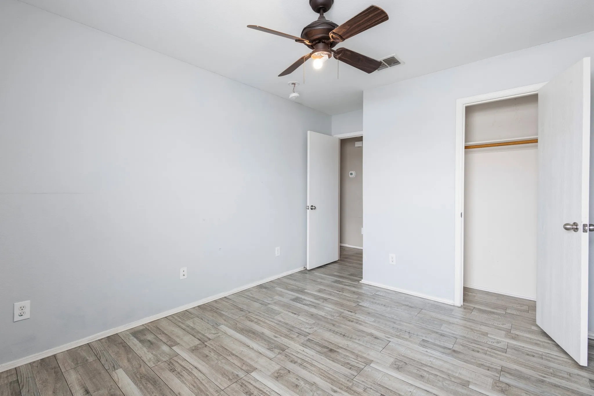 Wood-finish plank flooring, ceiling fan with integrated lighting, and a built-in closet with hanging rod