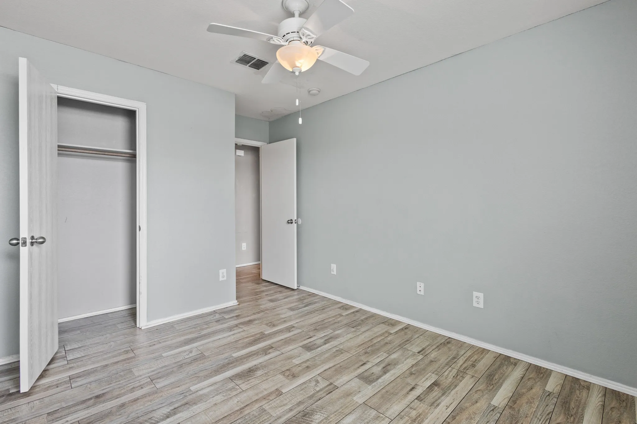 Wood-finish flooring, light grey wall paint, and a ceiling fan with integrated lighting