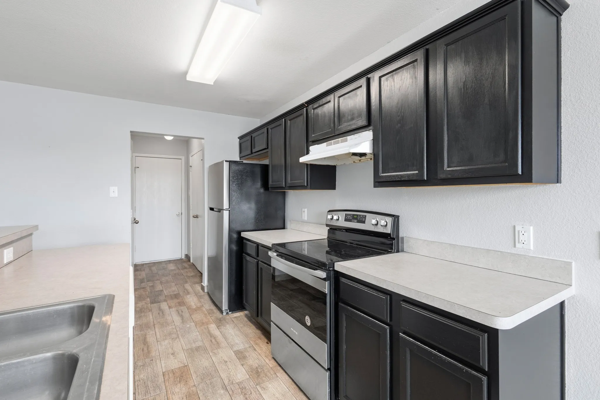 Kitchen featuring black cabinetry, stainless steel sink, light-toned countertops, and wood-finish flooring