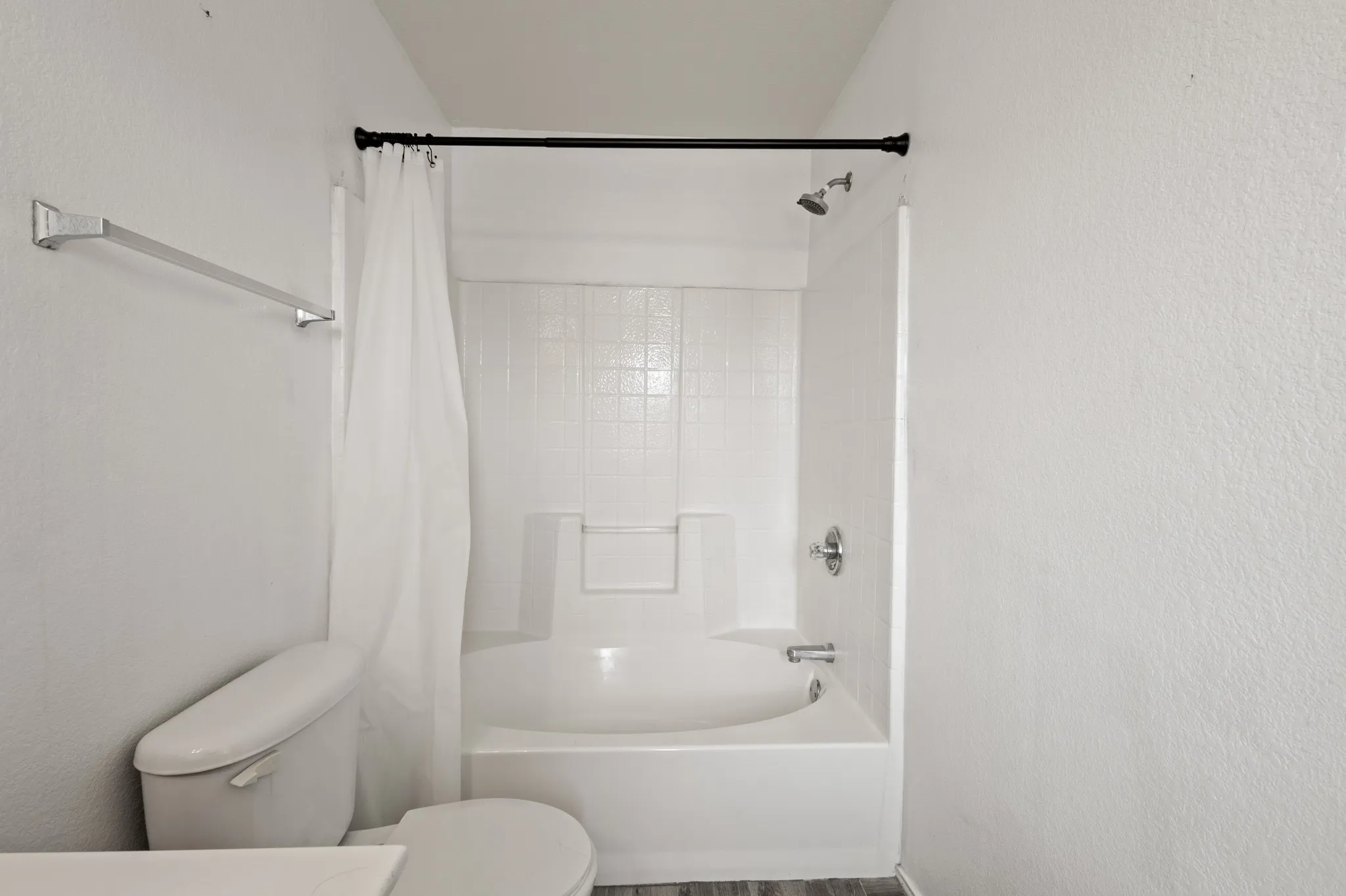 Bathtub with shower, white subway tile surround, chrome fixtures, and wood-finish flooring