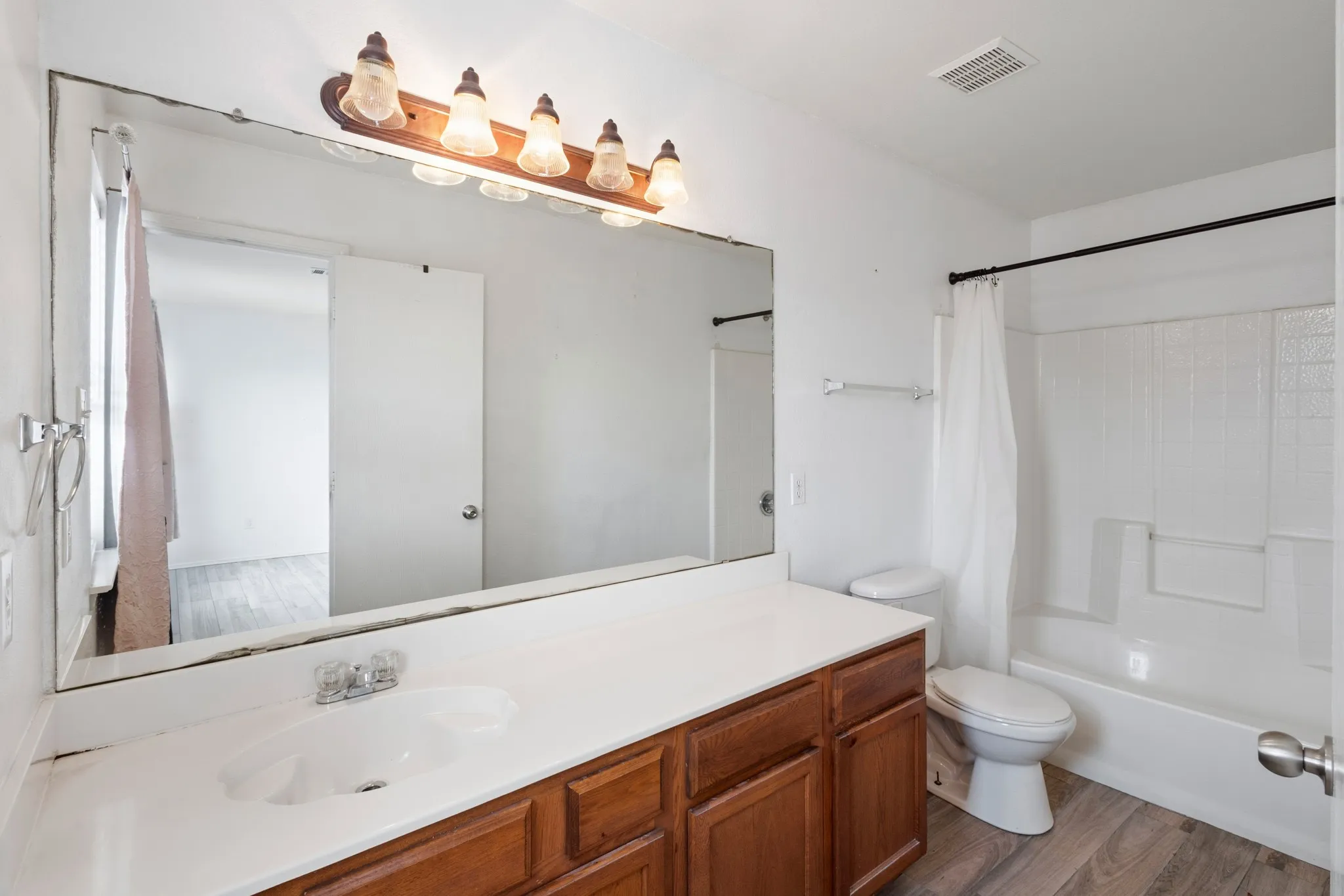 Wood-finish flooring, full vanity with integrated sink, large wall-mounted mirror, and a full bathtub with shower