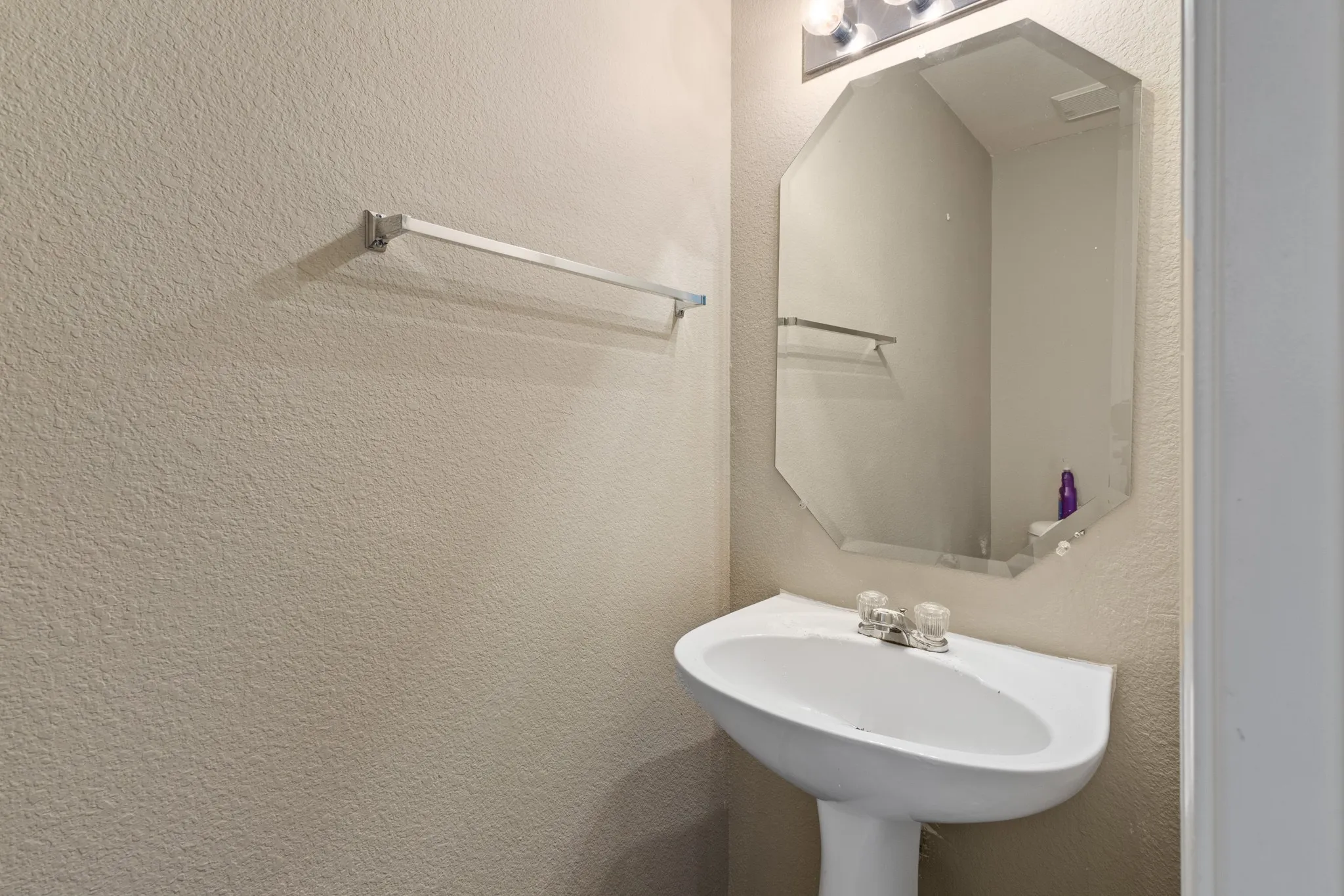 Pedestal sink with chrome faucet, octagonal wall-mounted mirror, and wall-mounted vanity lighting
