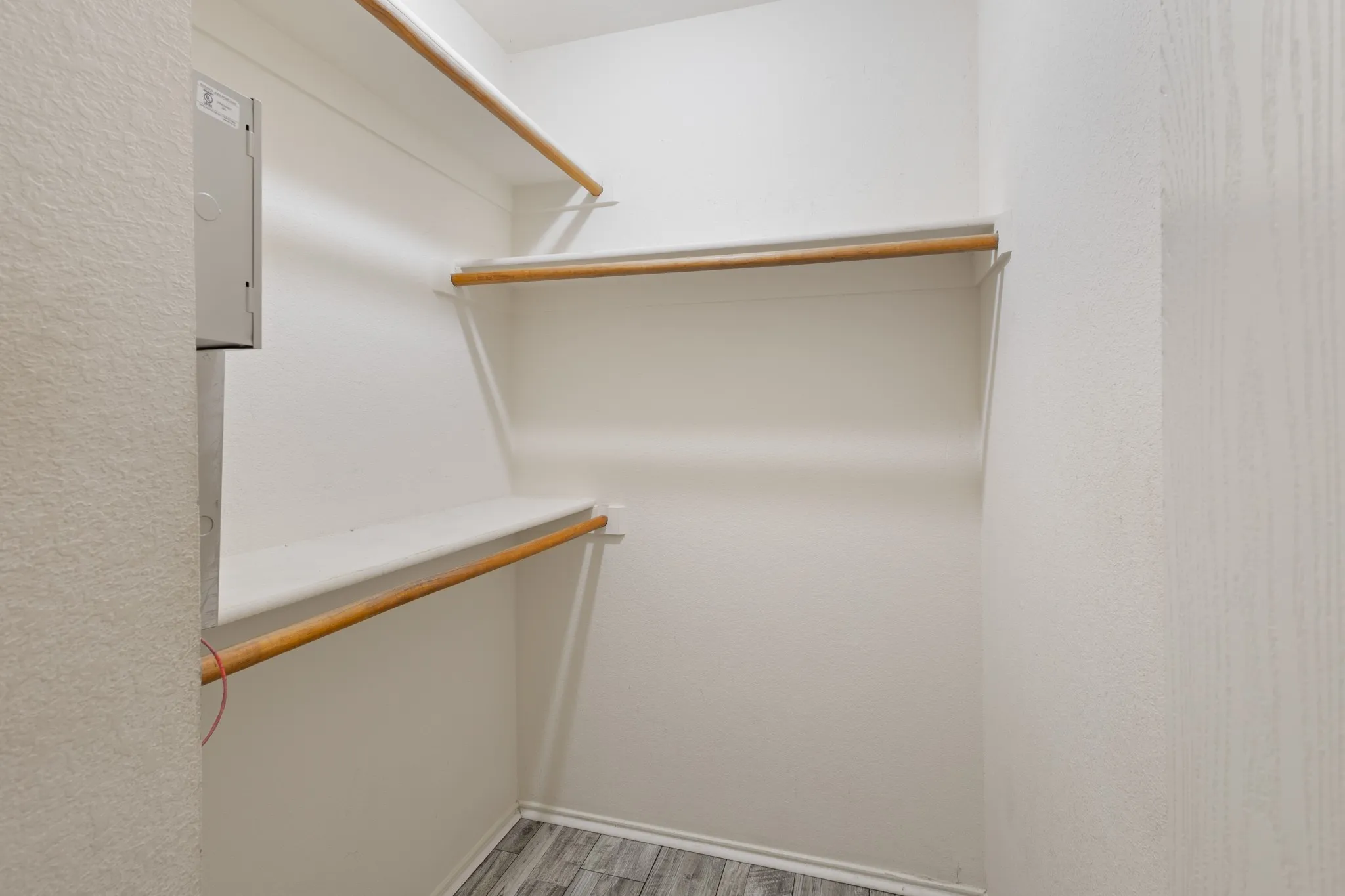 Walk-in closet with multiple shelving units, hanging rods, and wood-finish flooring