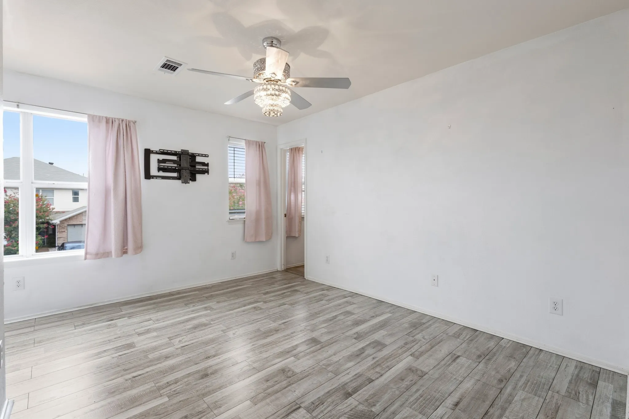 Wood-finish flooring, white walls, two windows, and a ceiling fan with integrated lighting
