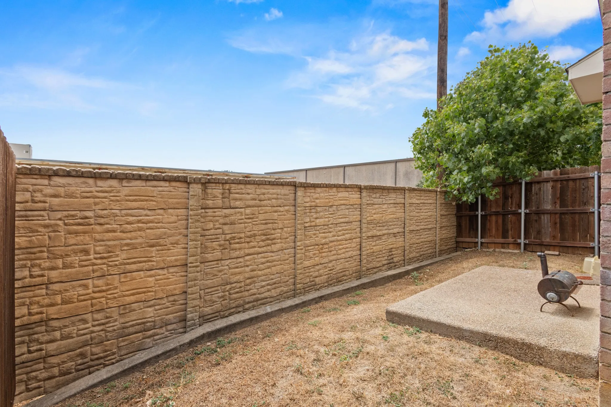 Backyard space featuring a concrete patio, stone-look privacy fence, and wood fence sections