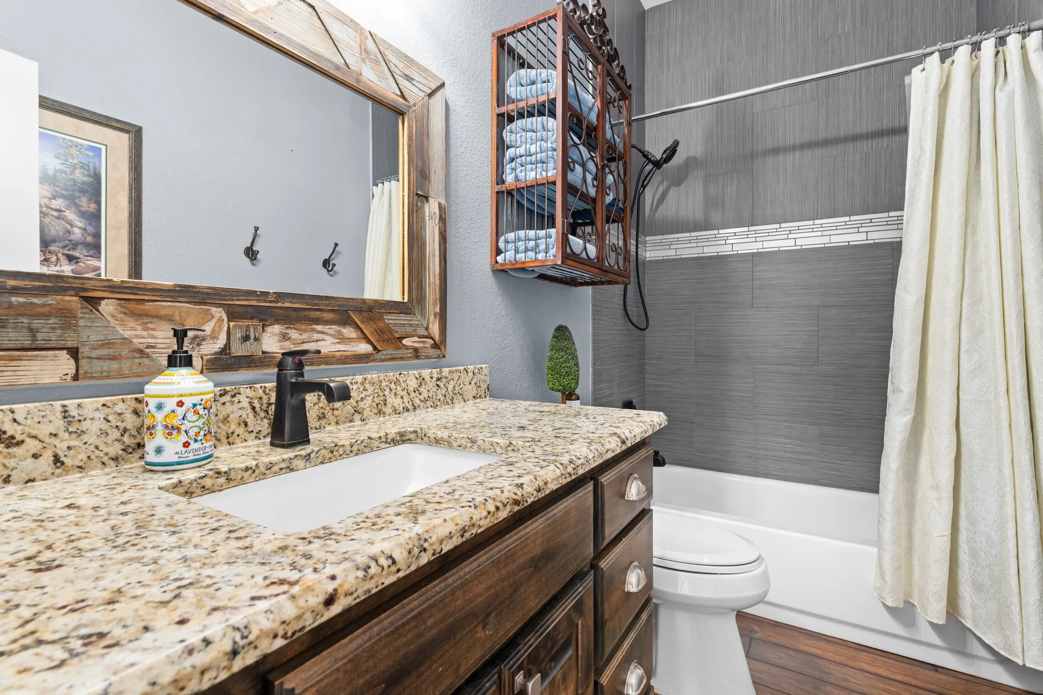 Granite countertop with undermount sink, dark wood-finish vanity, rustic wood-frame mirror, and dark-finish faucet