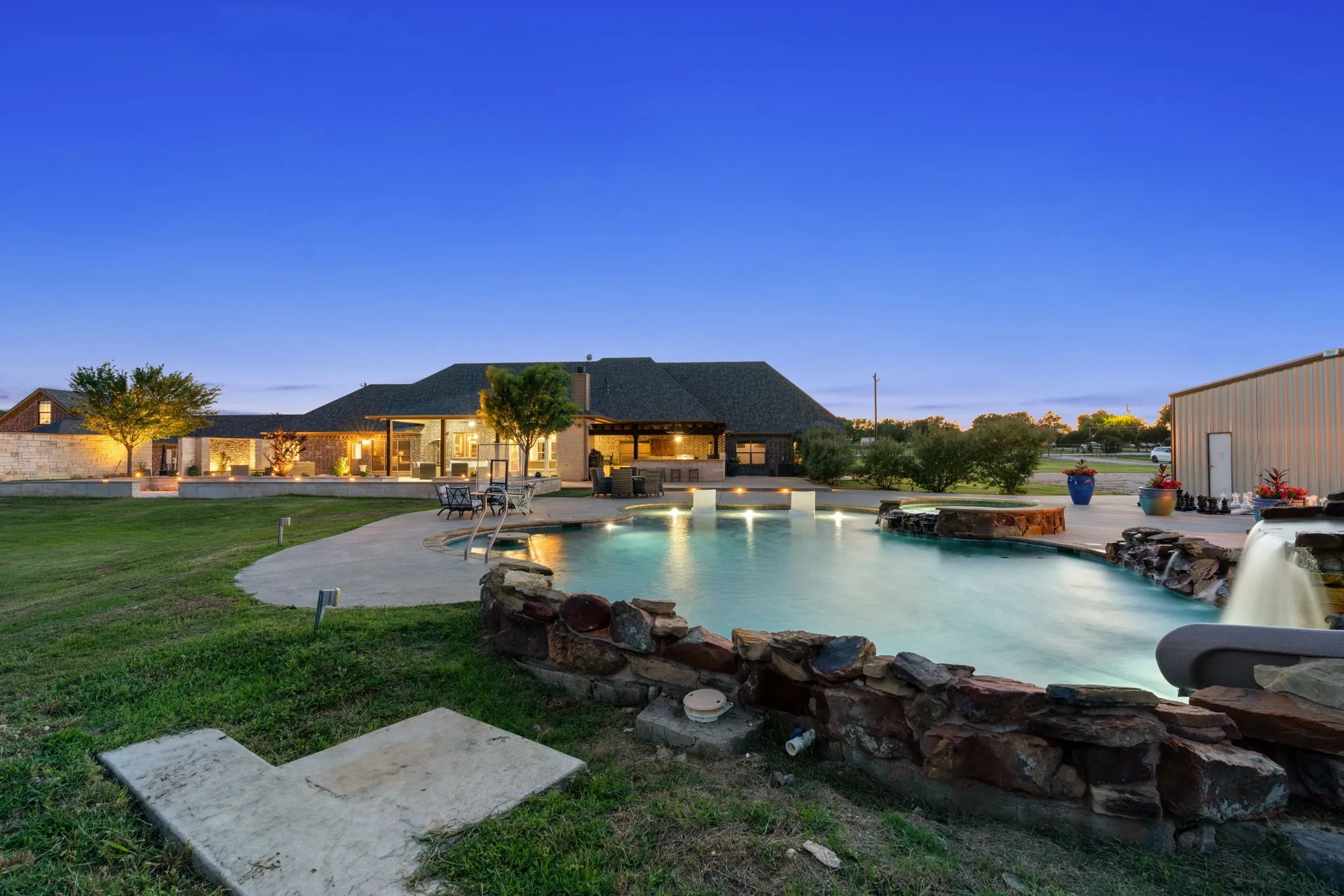 Expansive outdoor living area featuring a custom pool with rock accents, a separate spa, a waterfall feature, and a broad concrete patio