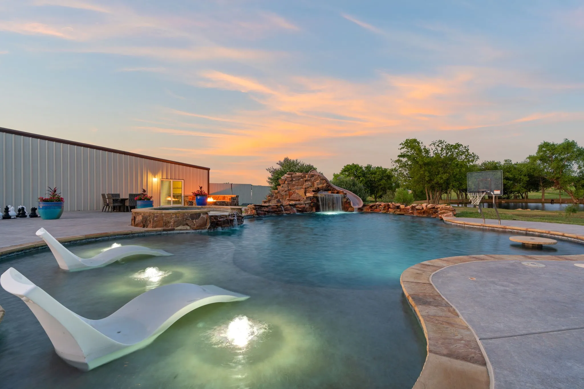 Custom-shaped swimming pool with an integrated rock waterfall, a waterslide, a built-in spa, and submerged seating areas