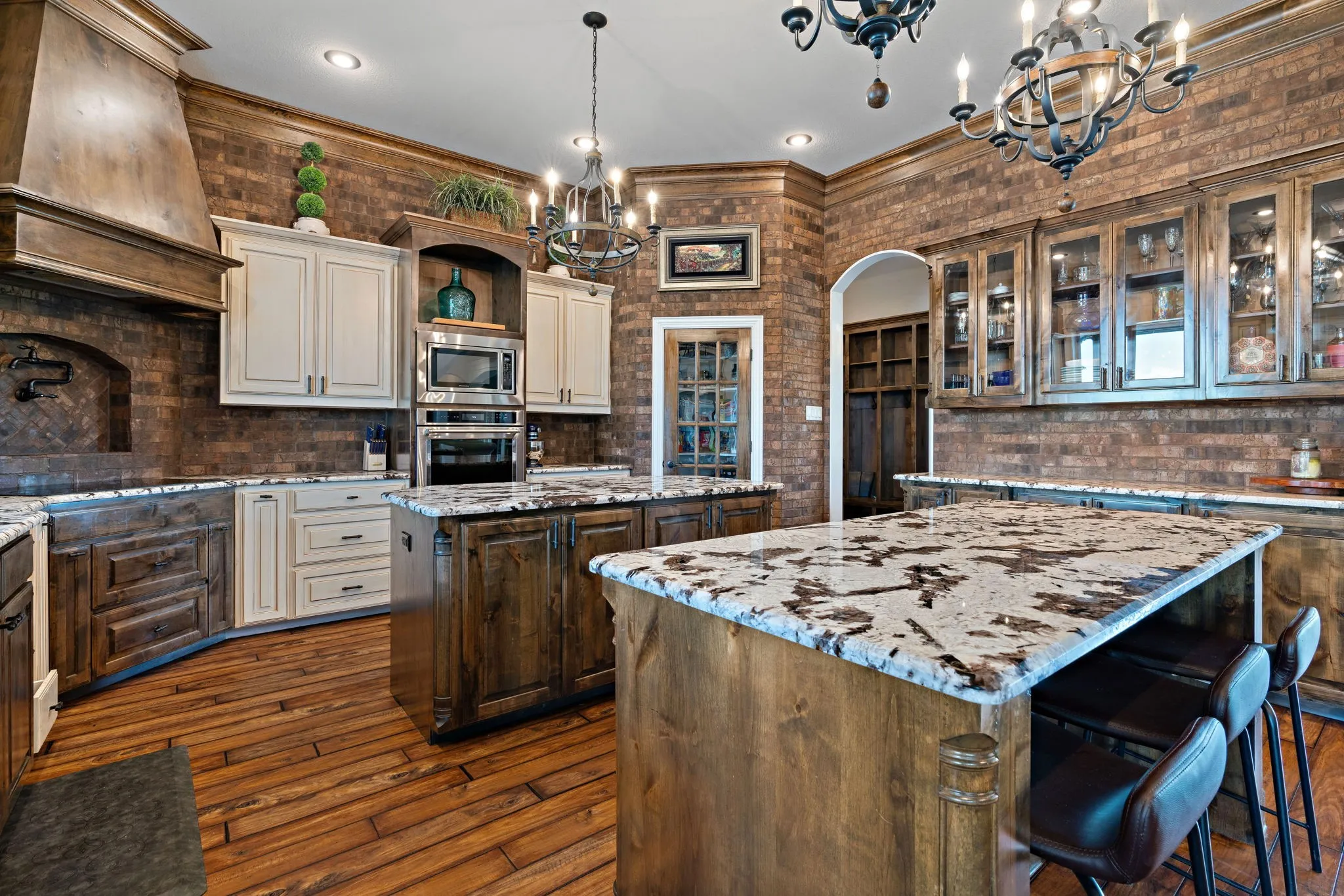 Kitchen featuring wood-finish flooring, two large islands with stone countertops, a decorative range hood, and built-in stainless steel appliances