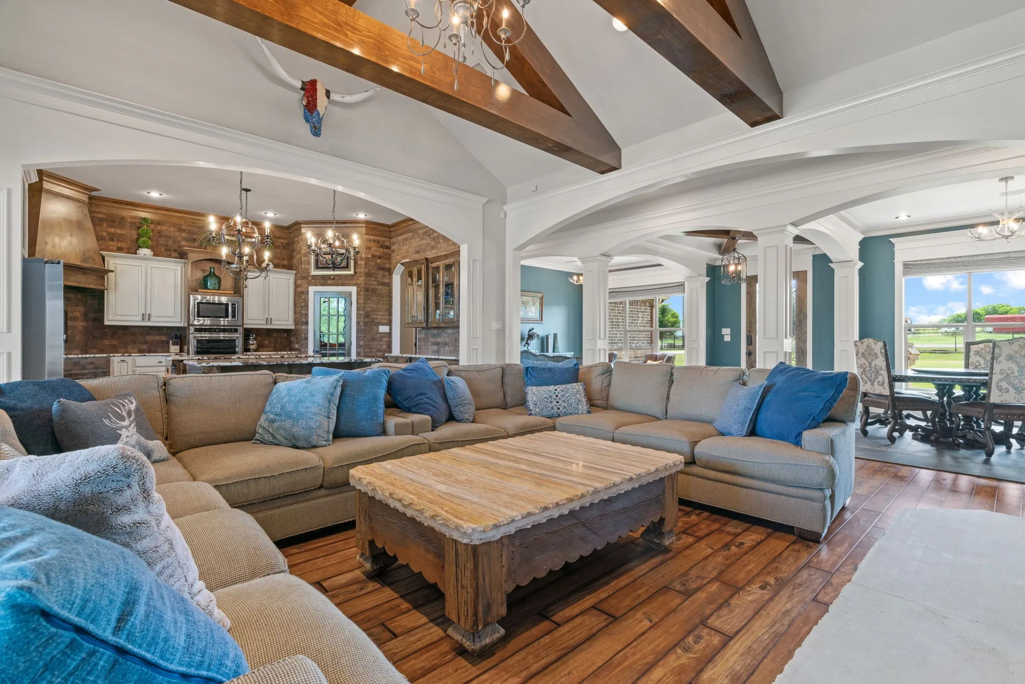 Vaulted ceiling with exposed wood beams, wood-finish flooring, recessed lighting, and a kitchen featuring a brick-finish backsplash and white cabinetry
