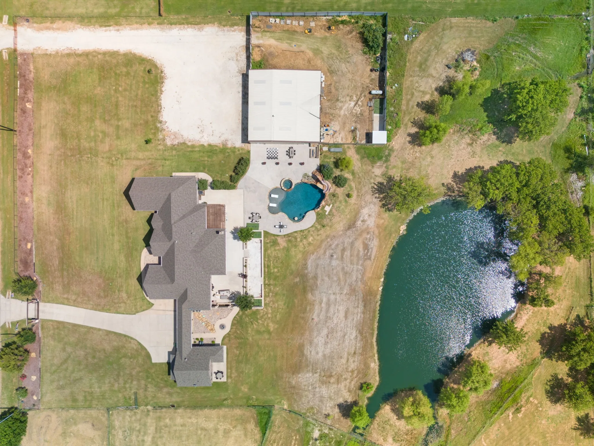 Expansive property featuring a large residence, private swimming pool with spa, concrete patio space, a dedicated outbuilding, and a private pond