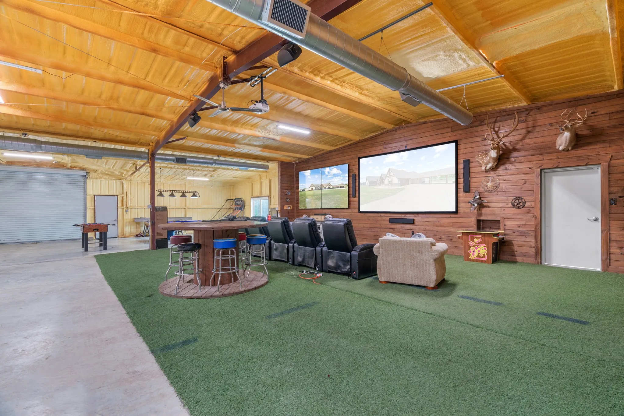 Enormous Shop- Expansive open space featuring a large projection screen, two additional wall-mounted screens, and a wood-paneled accent wall
