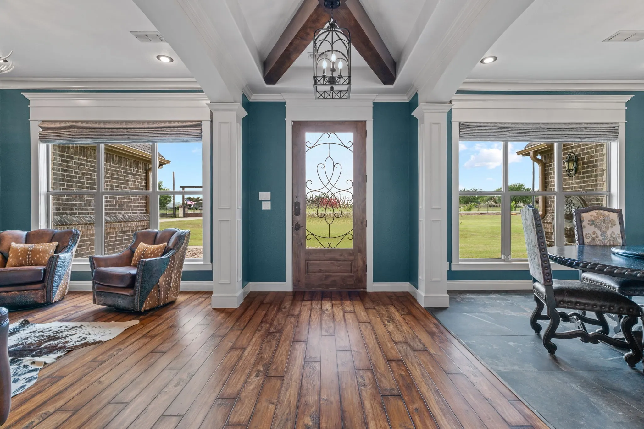 Wood-finish flooring, exposed ceiling beams, decorative front door with wrought iron detailing, recessed lighting, and large windows