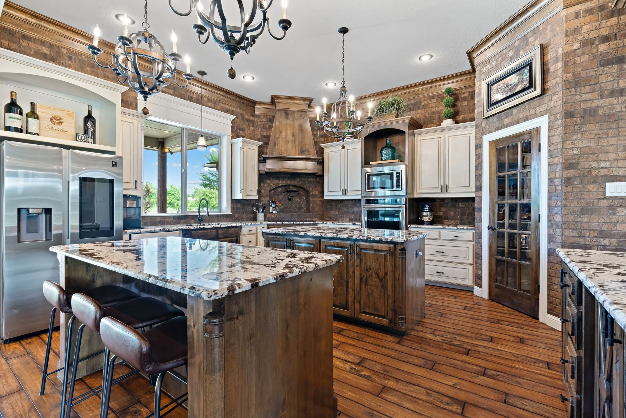 Vaulted ceiling with exposed wood beams, stone-faced fireplace with a hearth, wood-finish flooring, large windows, and a cased opening to the kitchen