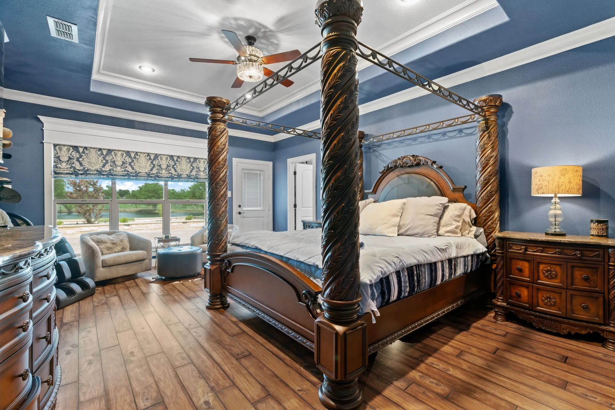 Tray ceiling with crown molding, wood-finish flooring, recessed lighting, ceiling fan with chandelier, and a large window