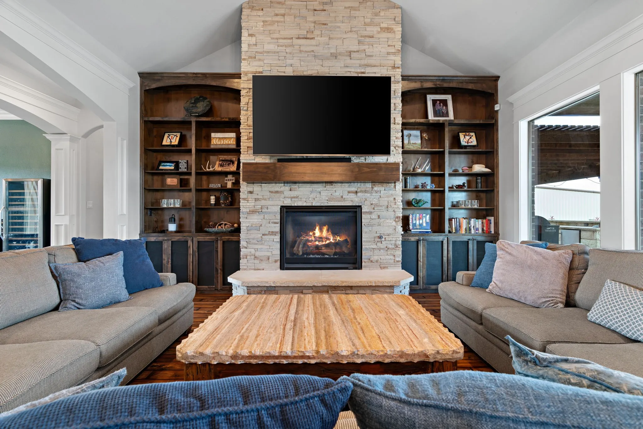 Stone-clad fireplace with a wood mantel, built-in shelving, vaulted ceiling, and wood-finish flooring