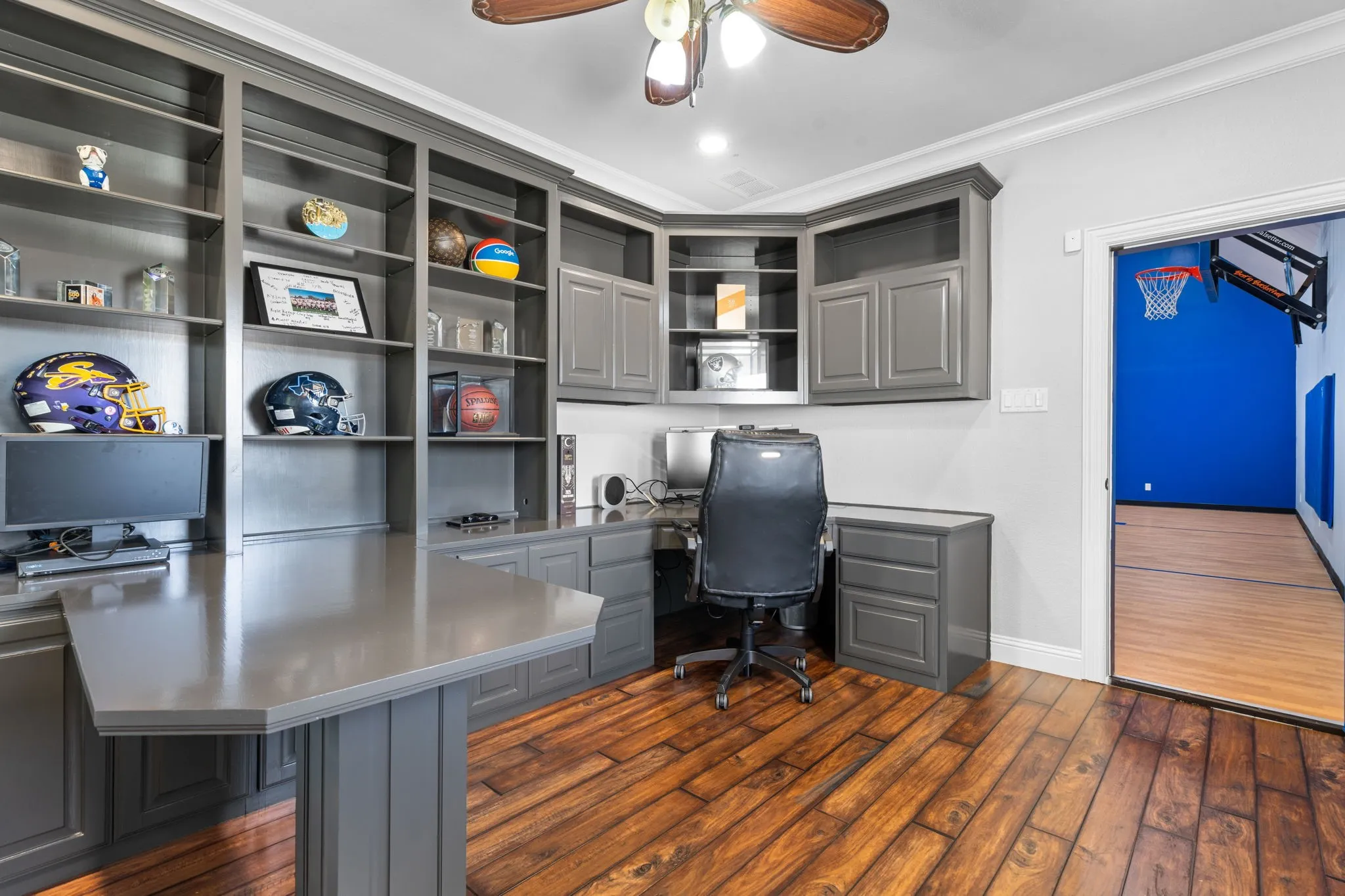 Wood-finish flooring with built-in cabinetry, integrated desk space, ceiling fan with light fixture, and crown molding