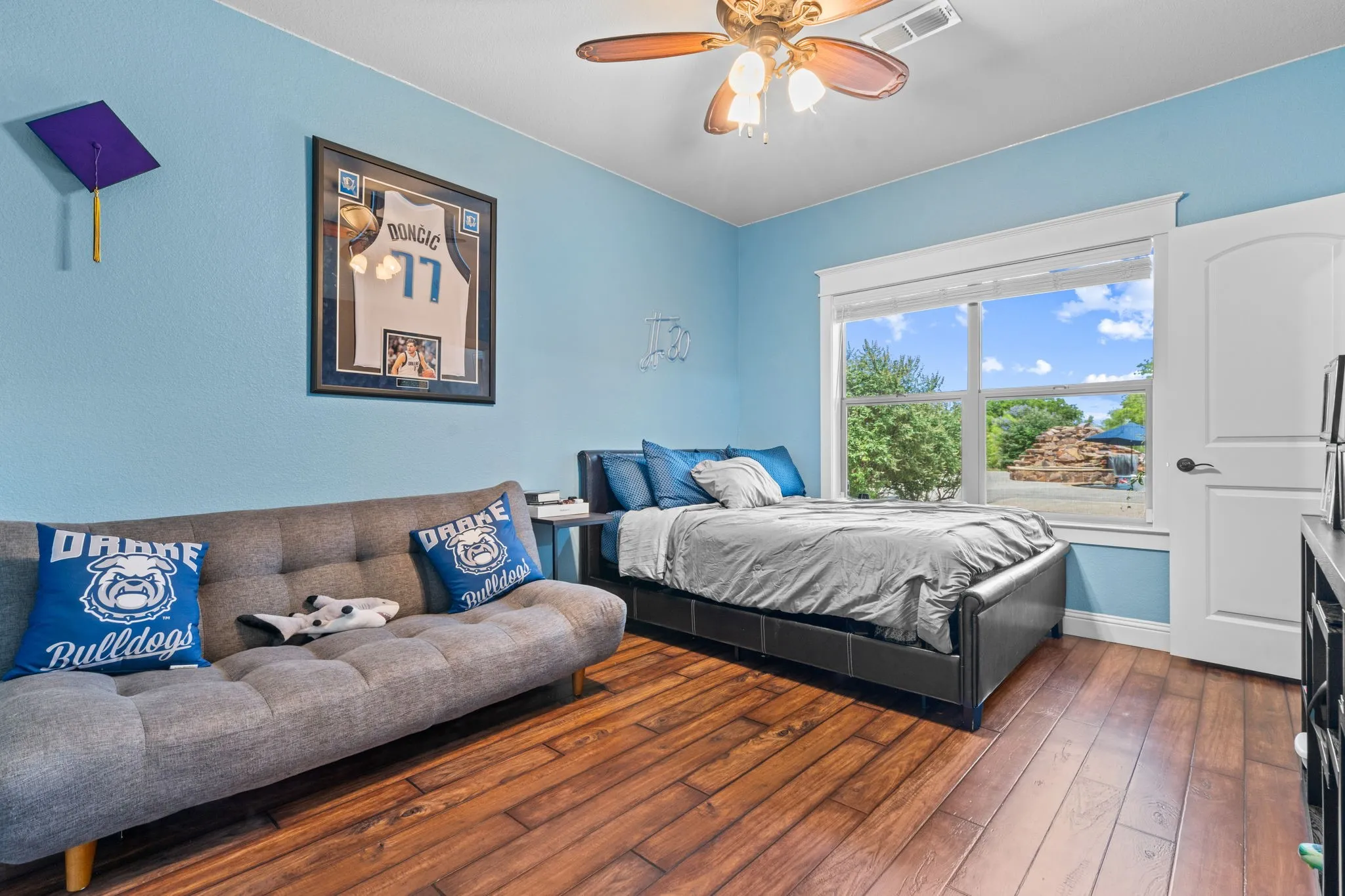 Wood-finish flooring, a ceiling fan with integrated lighting, and a window with white trim