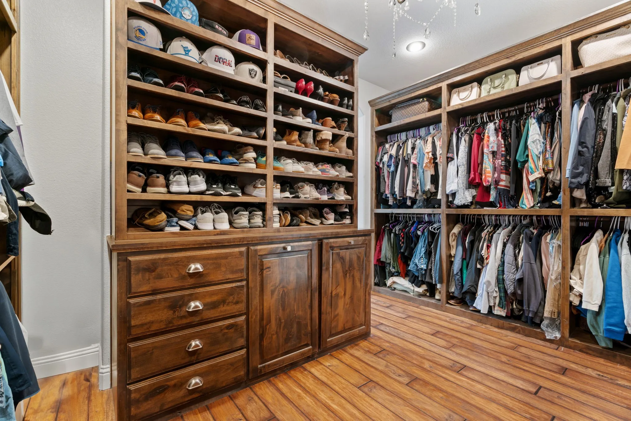 Primary closet- Custom built-in wood cabinetry, wood-finish flooring, recessed lighting, and a chandelier fixture