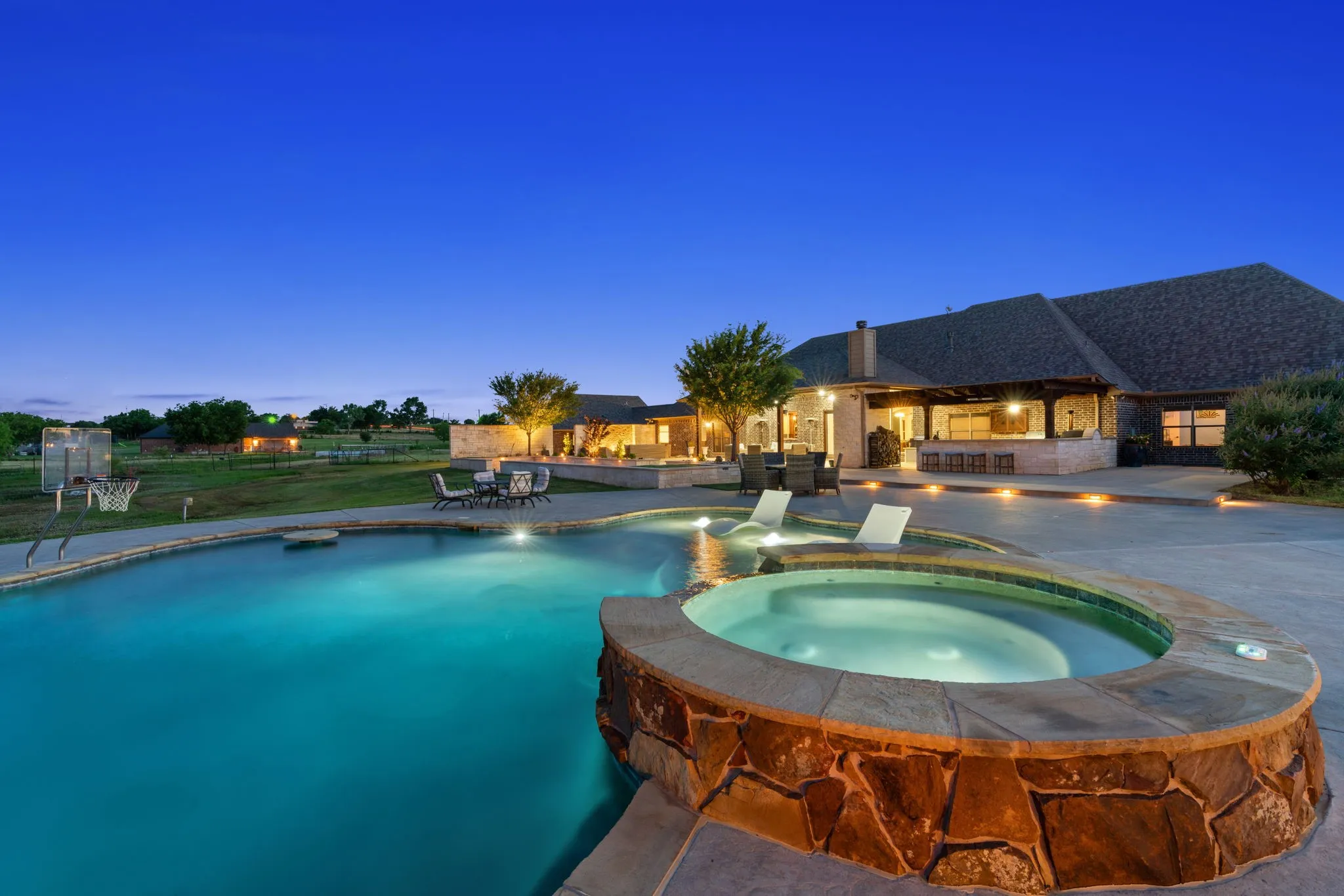 Expansive concrete patio with an in-ground swimming pool, an integrated stone-clad spa, and an outdoor kitchen with bar​​‌​​​​‌​​‌‌​‌‌​​​‌‌​‌​‌​‌​​​‌​​ seating
