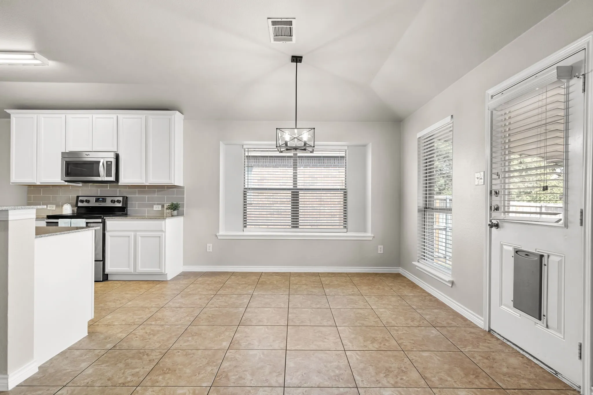 Kitchen and dining area featuring white cabinetry, stainless steel appliances, a subway tile backsplash, and tile flooring