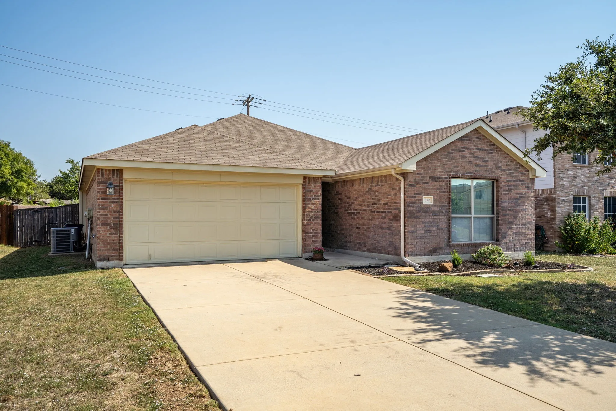 Brick exterior with an attached garage, concrete driveway, and established landscaping