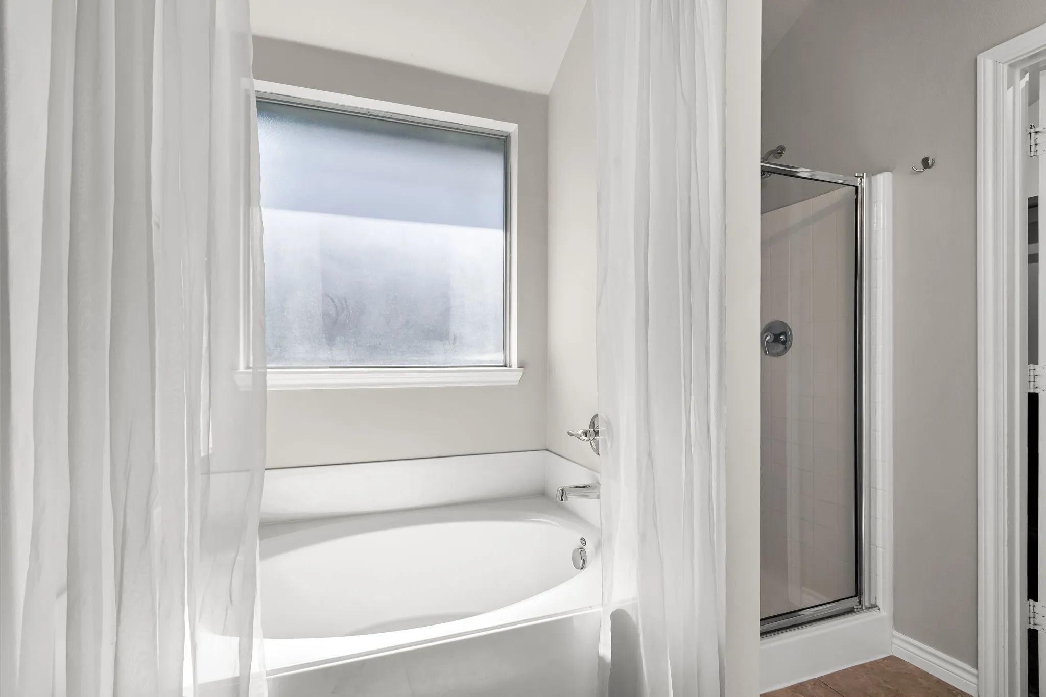 Window-equipped soaking tub with chrome fixtures, complemented by a glass-enclosed shower with chrome hardware
