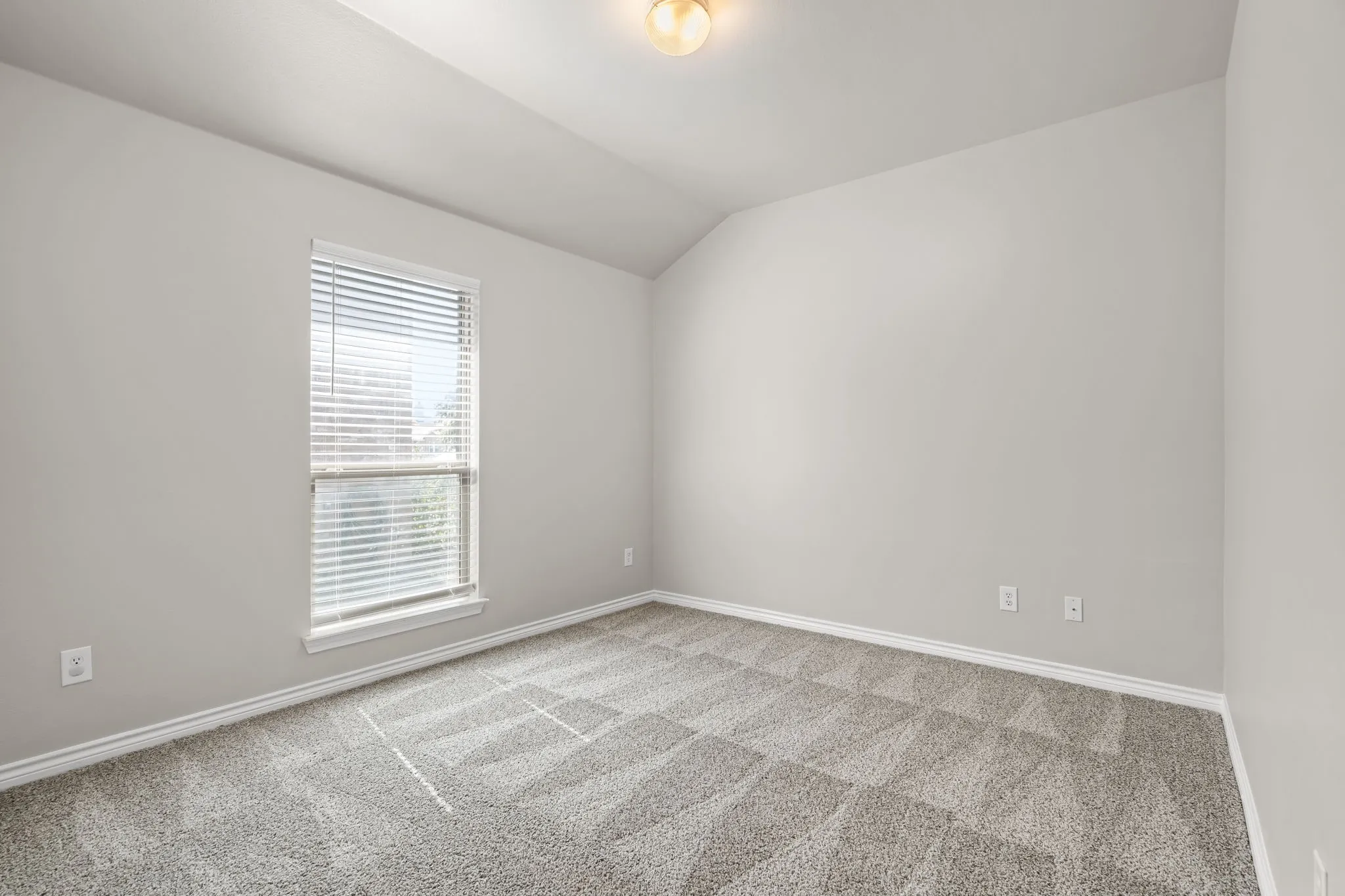 Light-toned walls, sloped ceiling, window with blinds, overhead lighting fixture, and gray patterned carpet