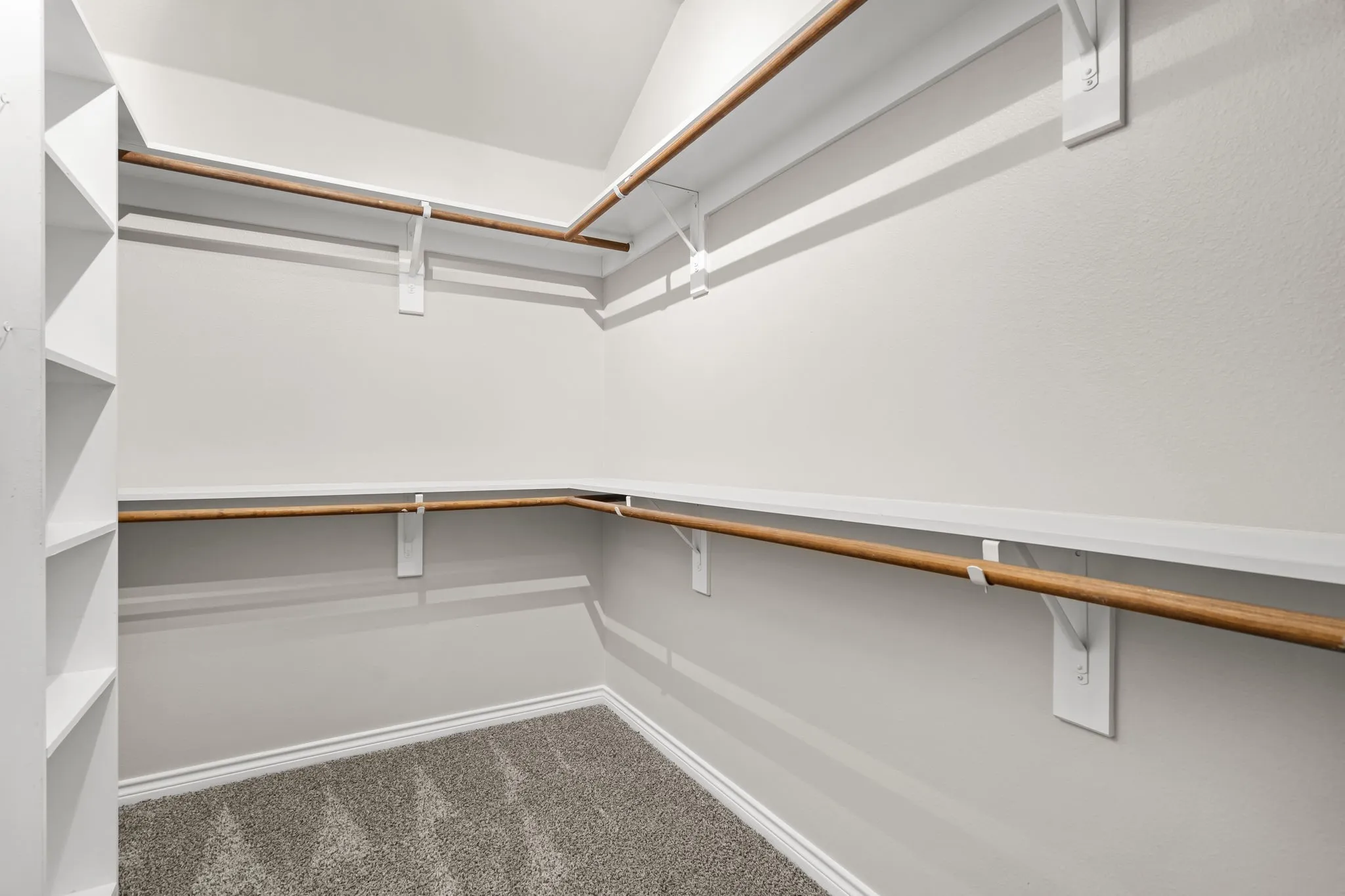 Walk-in closet with built-in shelving, multiple hanging rods, durable carpeting, and white trim