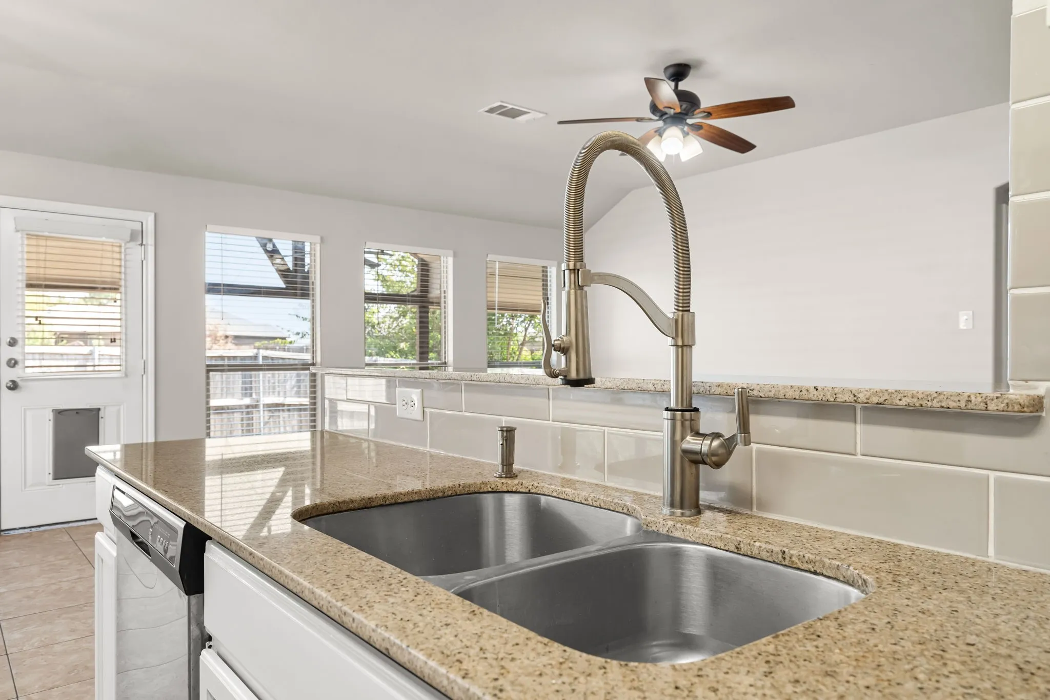 Dual basin stainless steel sink with a high-arch brushed nickel faucet, light-toned speckled countertops, and a subway tile backsplash