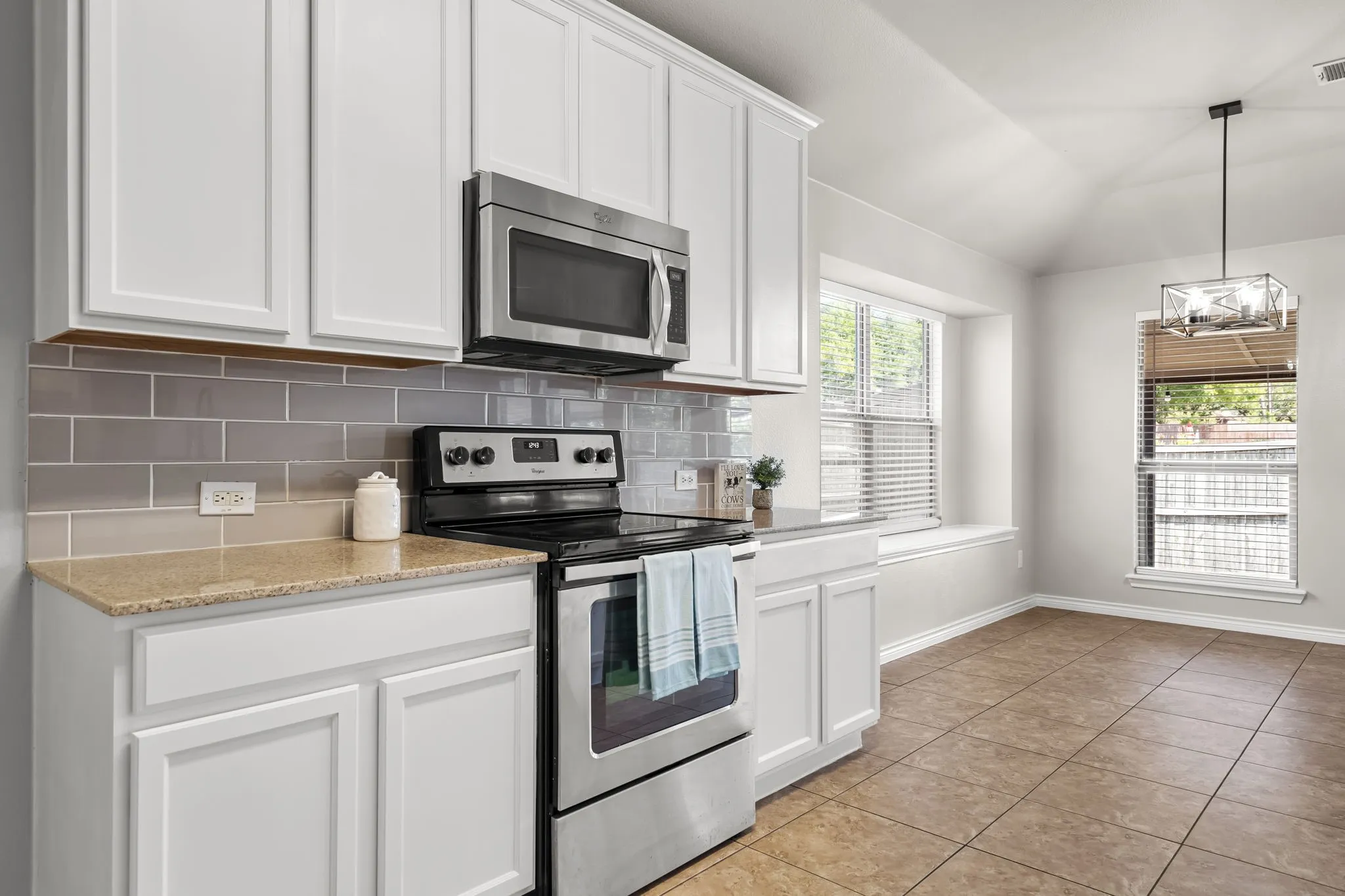 White shaker-style cabinetry, stainless steel appliances, subway tile backsplash, granite-finish countertops, and ceramic tile flooring