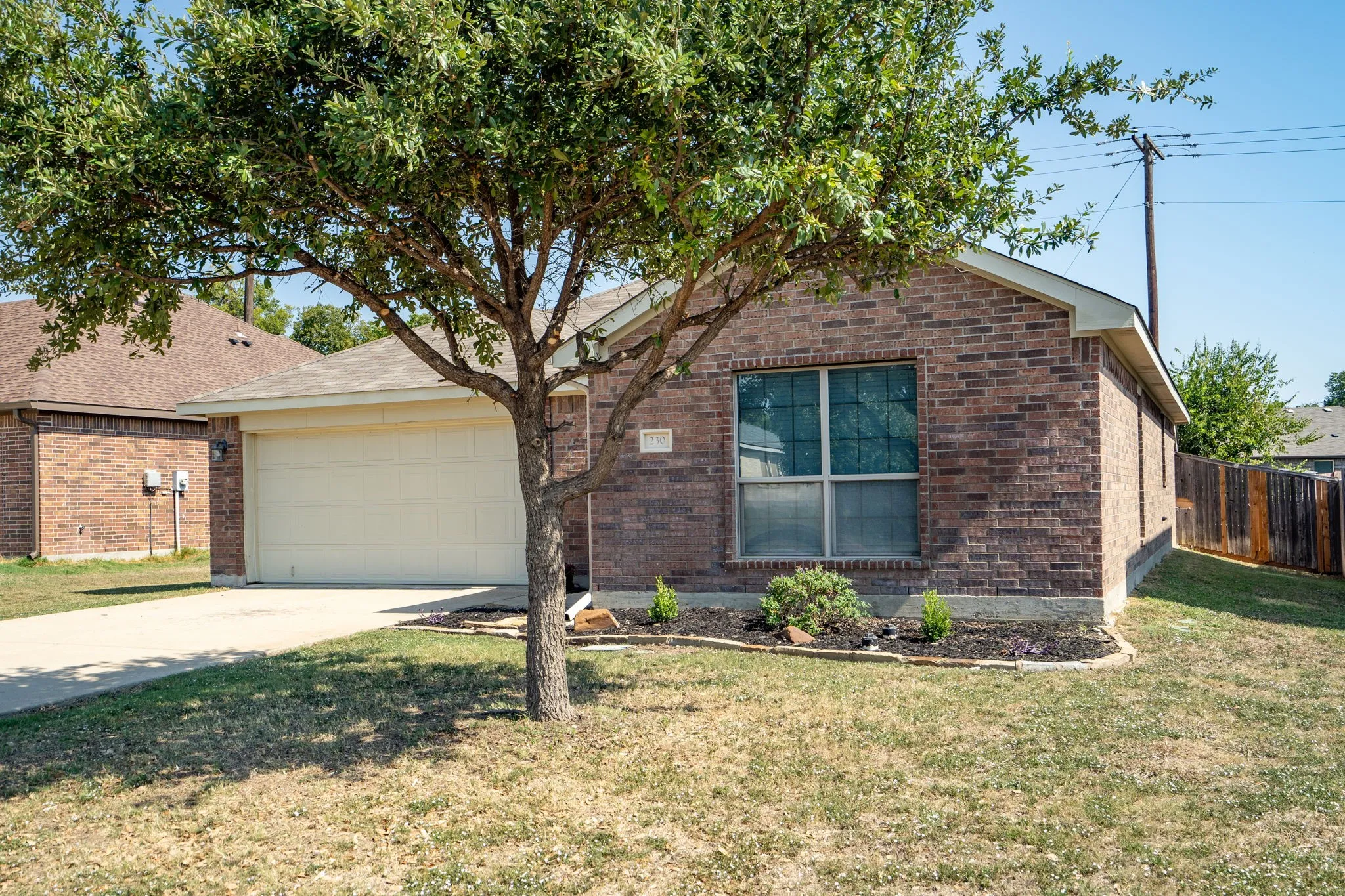 Brick exterior with a gabled roofline, front-facing garage, concrete driveway, and front landscaping