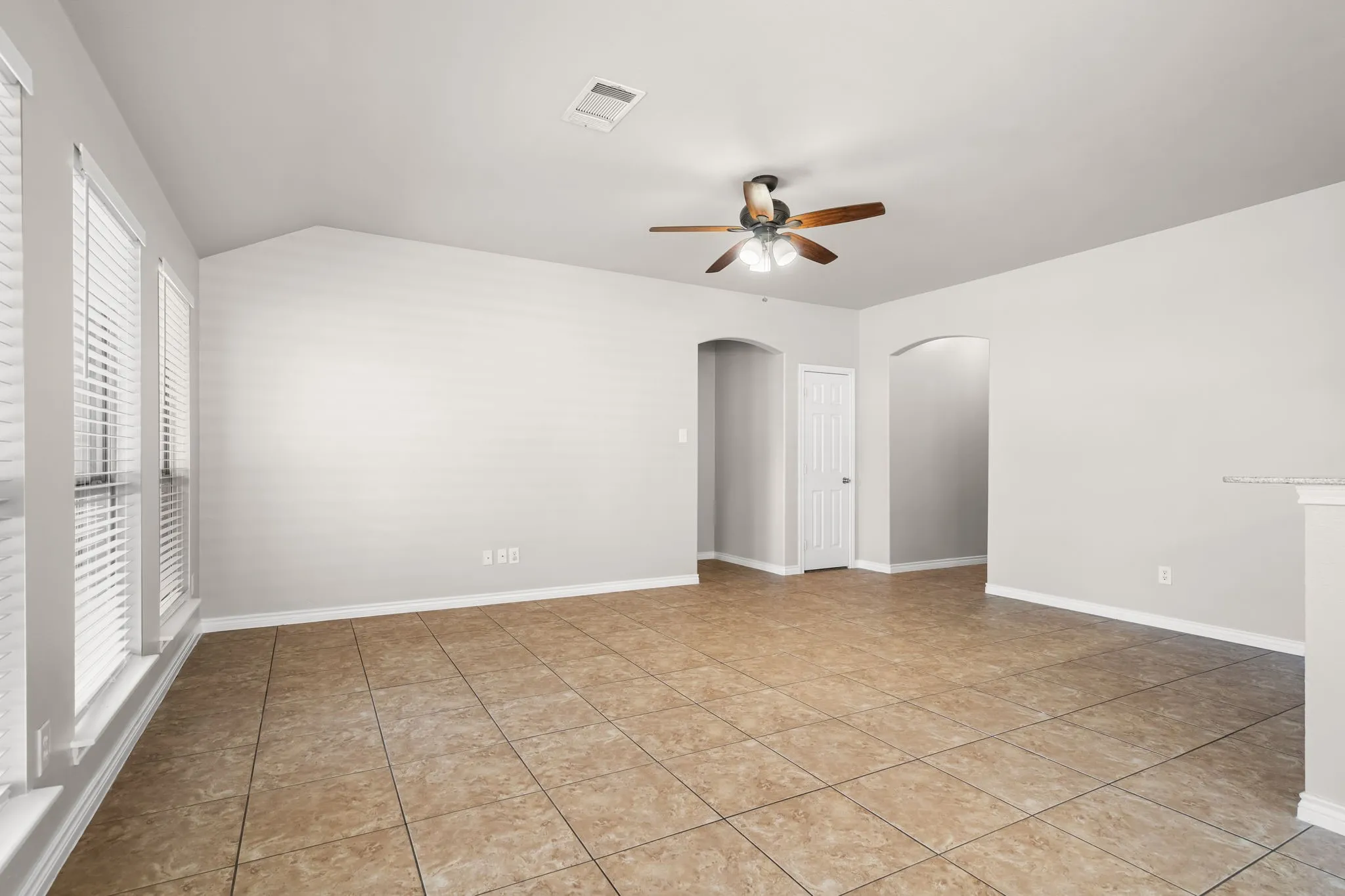 Vaulted ceiling, tiled flooring, arched doorways, multiple windows with blinds, and a ceiling fan with integrated lighting