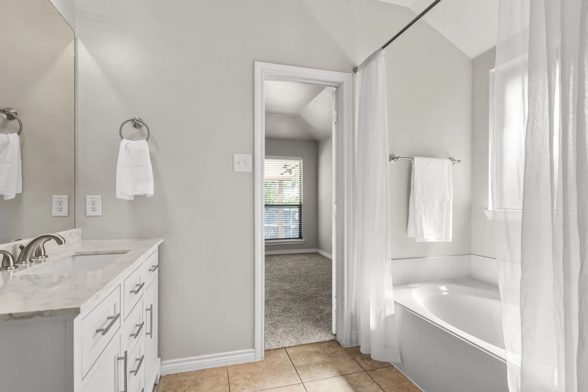 Bathroom featuring a built-in bathtub, a single vanity with a solid surface countertop, tile flooring, and a vaulted ceiling