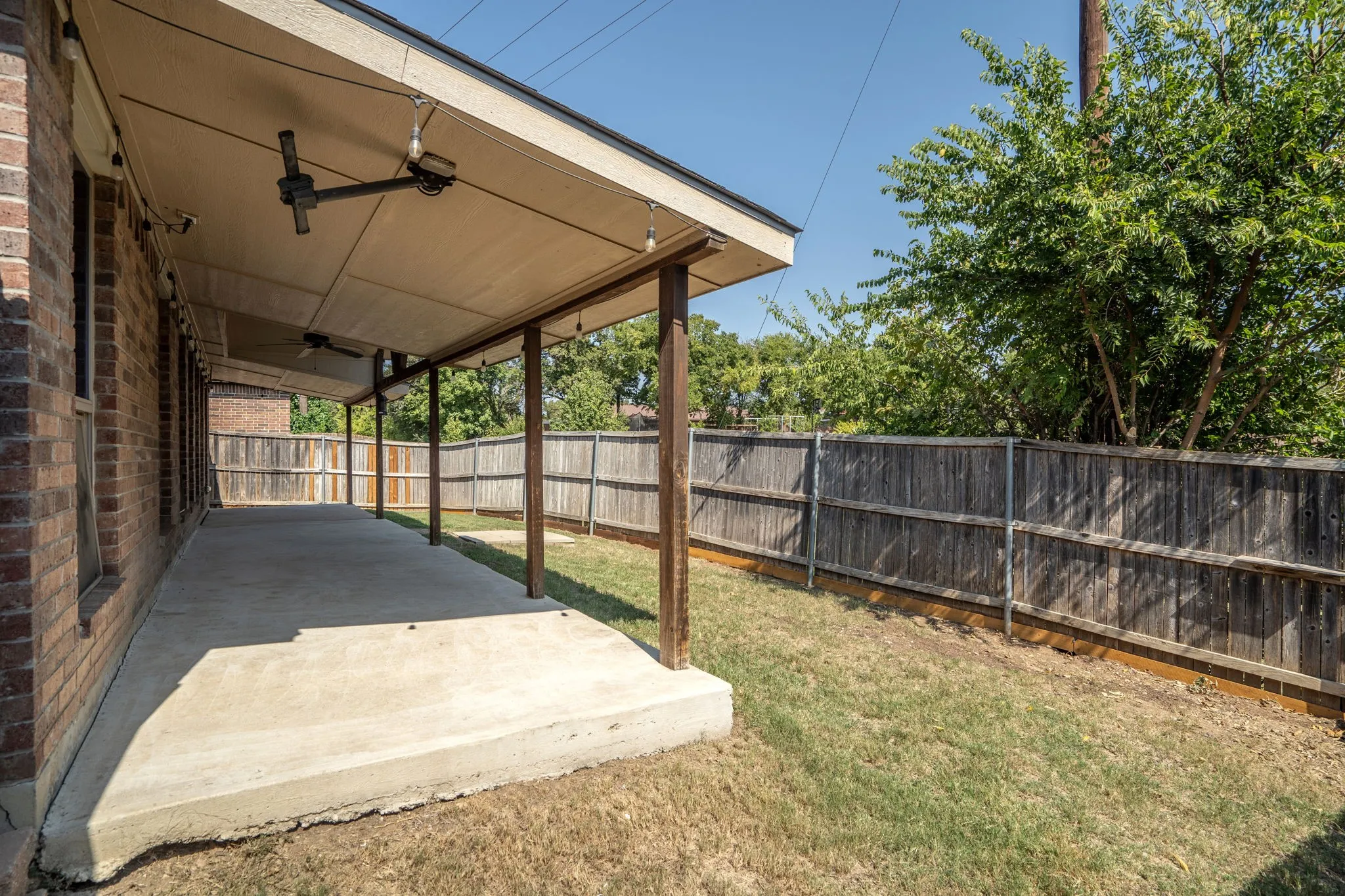 Expansive covered patio featuring two ceiling fans and string lighting, supported by multiple columns, with a concrete surface