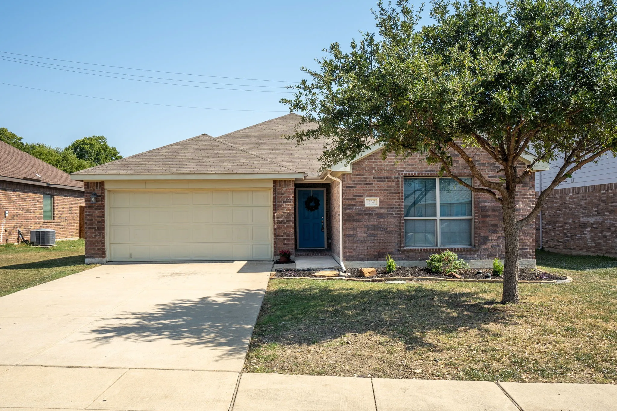 Brick exterior with an attached garage, paved driveway, and mature landscaping