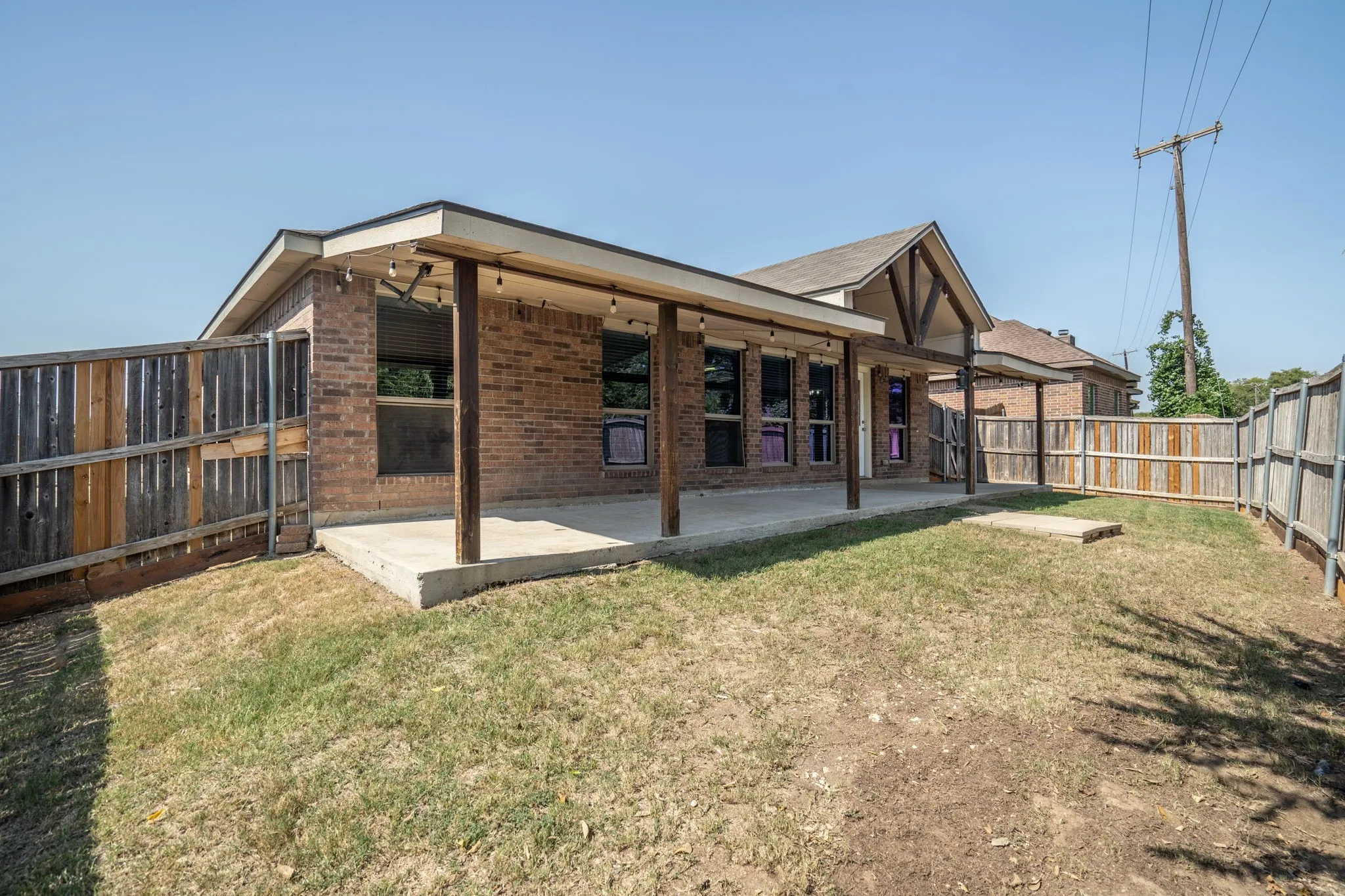 Brick exterior with a covered patio, concrete slab, and wood privacy fencing