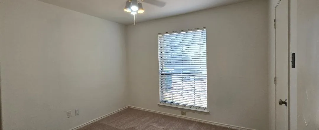 Carpeted flooring, window with blinds, ceiling fan with integrated lighting, and a white interior door
