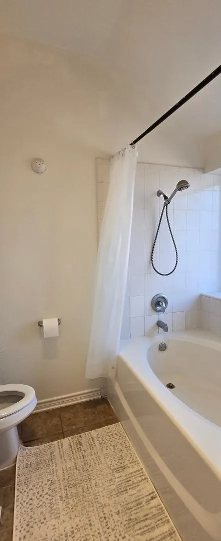 White tiled shower surround with a built-in tub, polished chrome fixtures, and a handheld showerhead